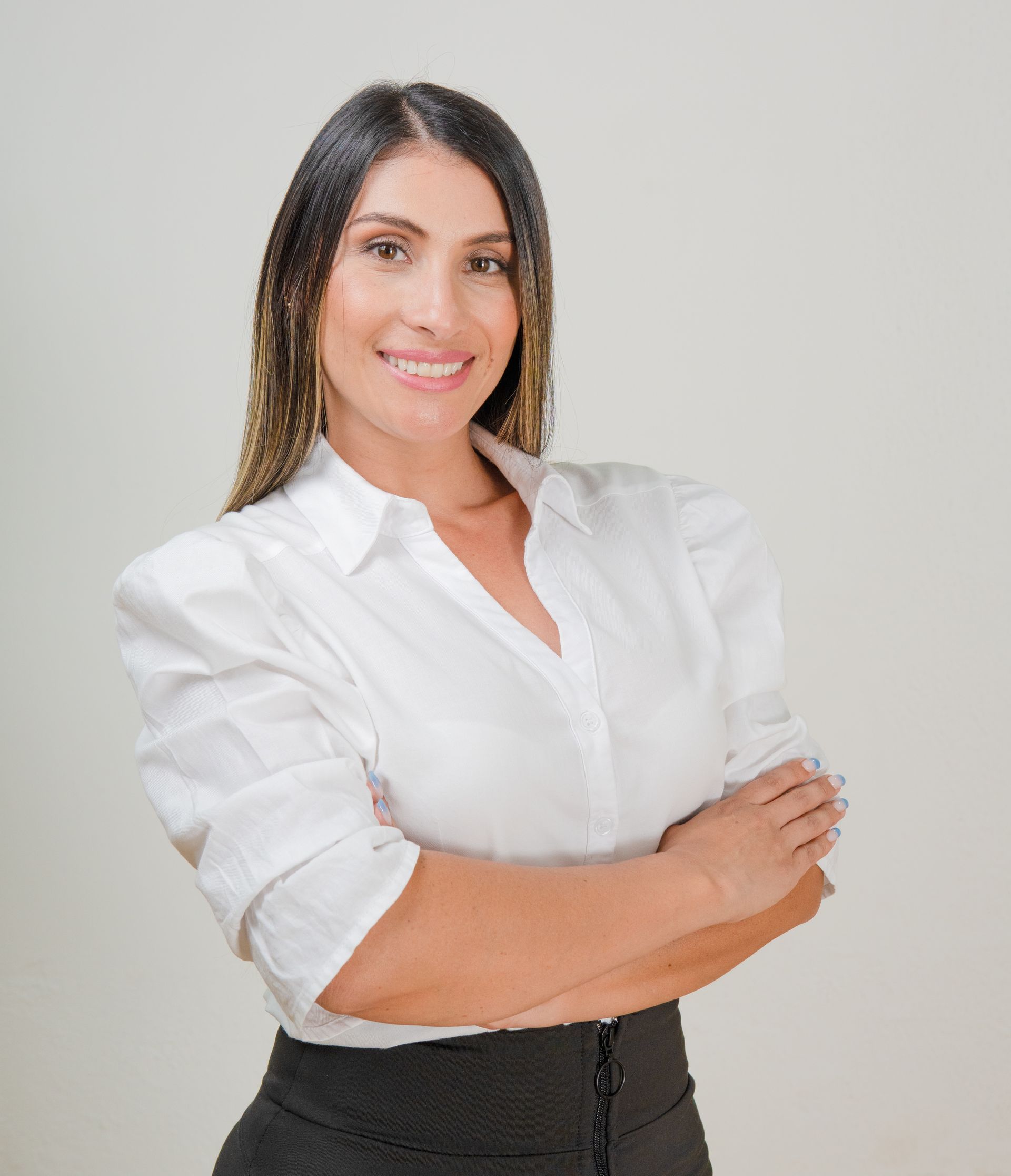 Mujer vestida con camisa blanca y falda negra, con los brazos cruzados, sonriendo.