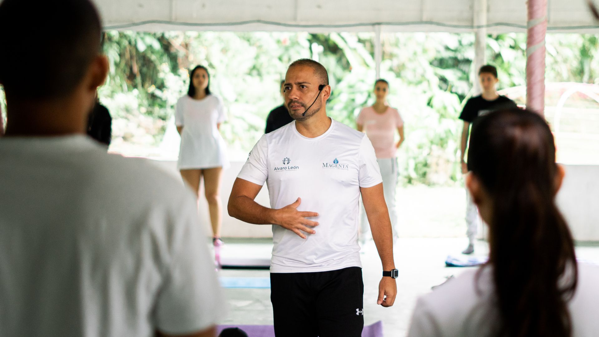 El instructor dirige la clase de ejercicios al aire libre, señalando el abdomen. Otros se ponen de pie y siguen la clase.
