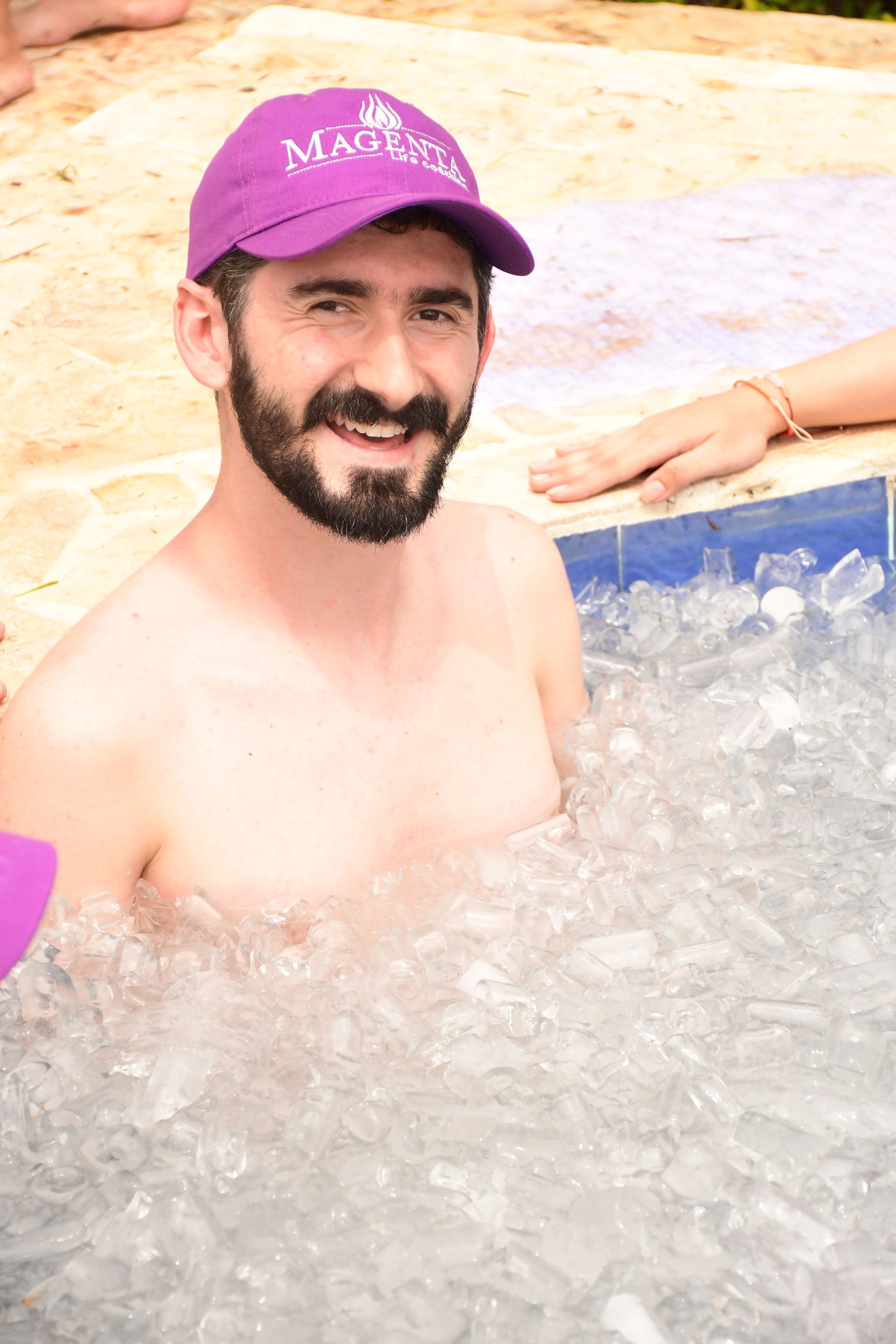 Un hombre con una gorra violeta sonríe mientras está sentado en una bañera llena de hielo.