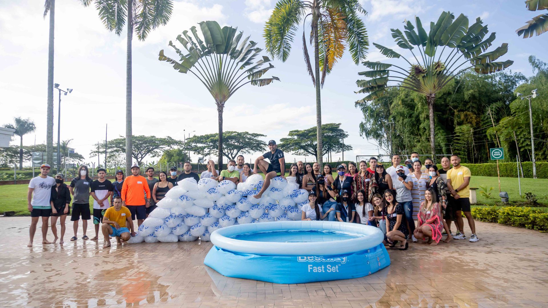 Grupo de personas posando con globos y una piscina para niños al aire libre en un parque.
