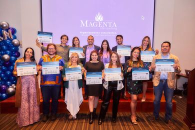 Grupo sosteniendo certificados en un salón con un fondo de logotipo magenta.