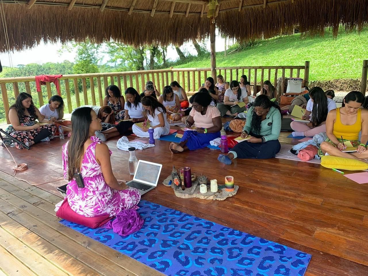 Grupo de personas en una reunión al aire libre con un presentador, una computadora portátil, tapetes y aceites esenciales.