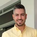 Hombre con cabello canoso sonriendo, vistiendo una camisa amarilla abotonada.