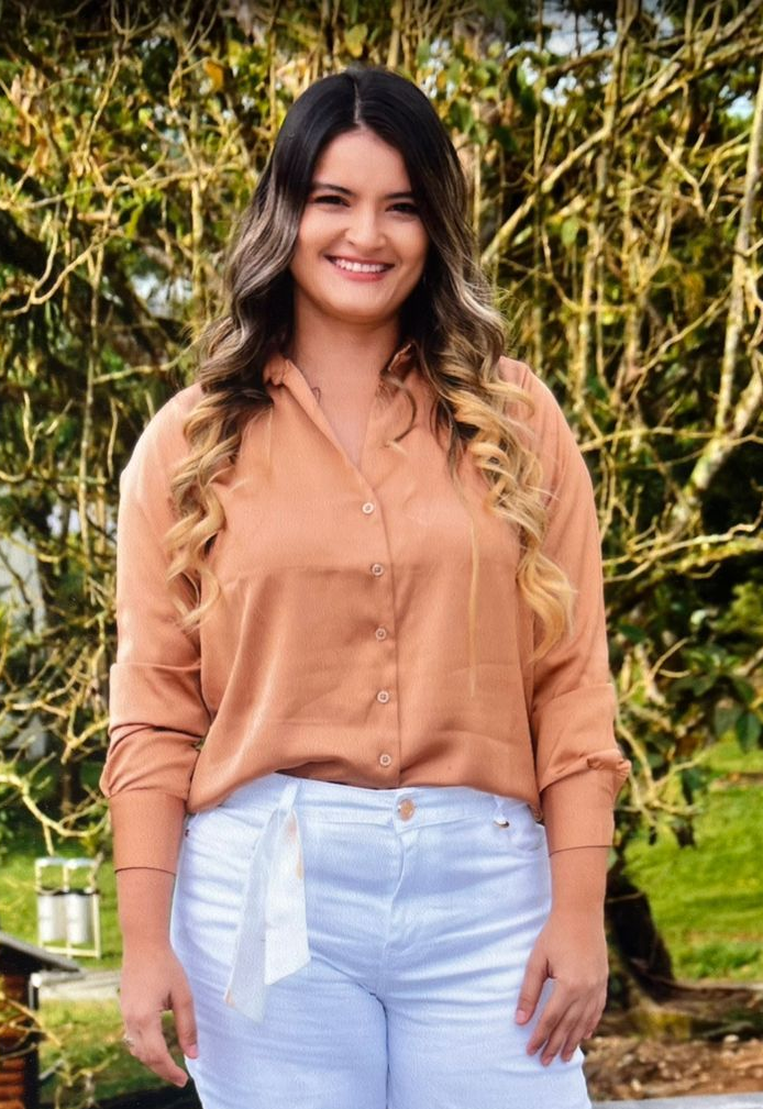 Mujer con una camisa abotonada de color óxido y pantalones blancos, sonriendo al aire libre.