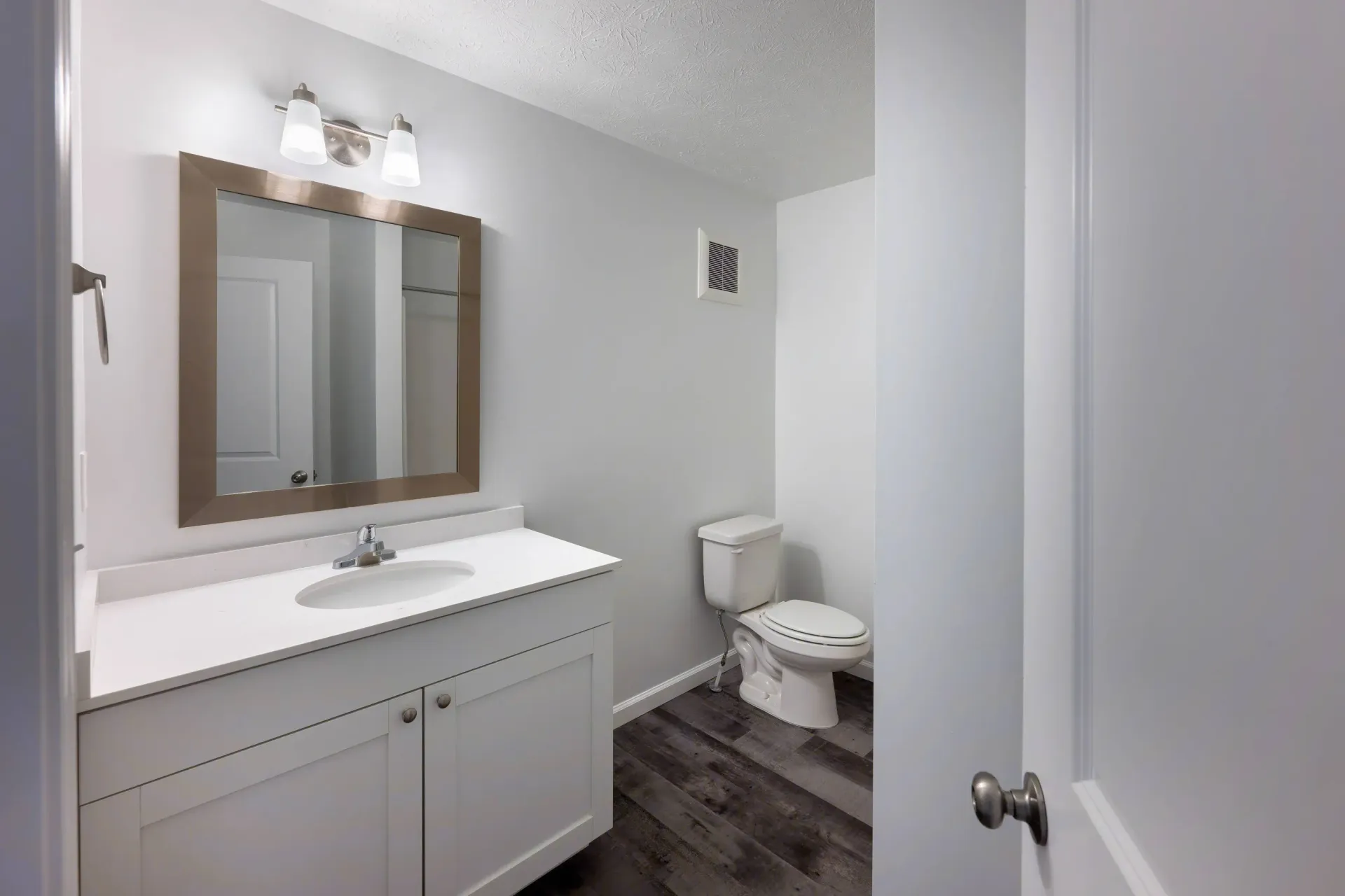 Bathroom with white vanity, mirror, light fixture, and toilet in a modern apartment.