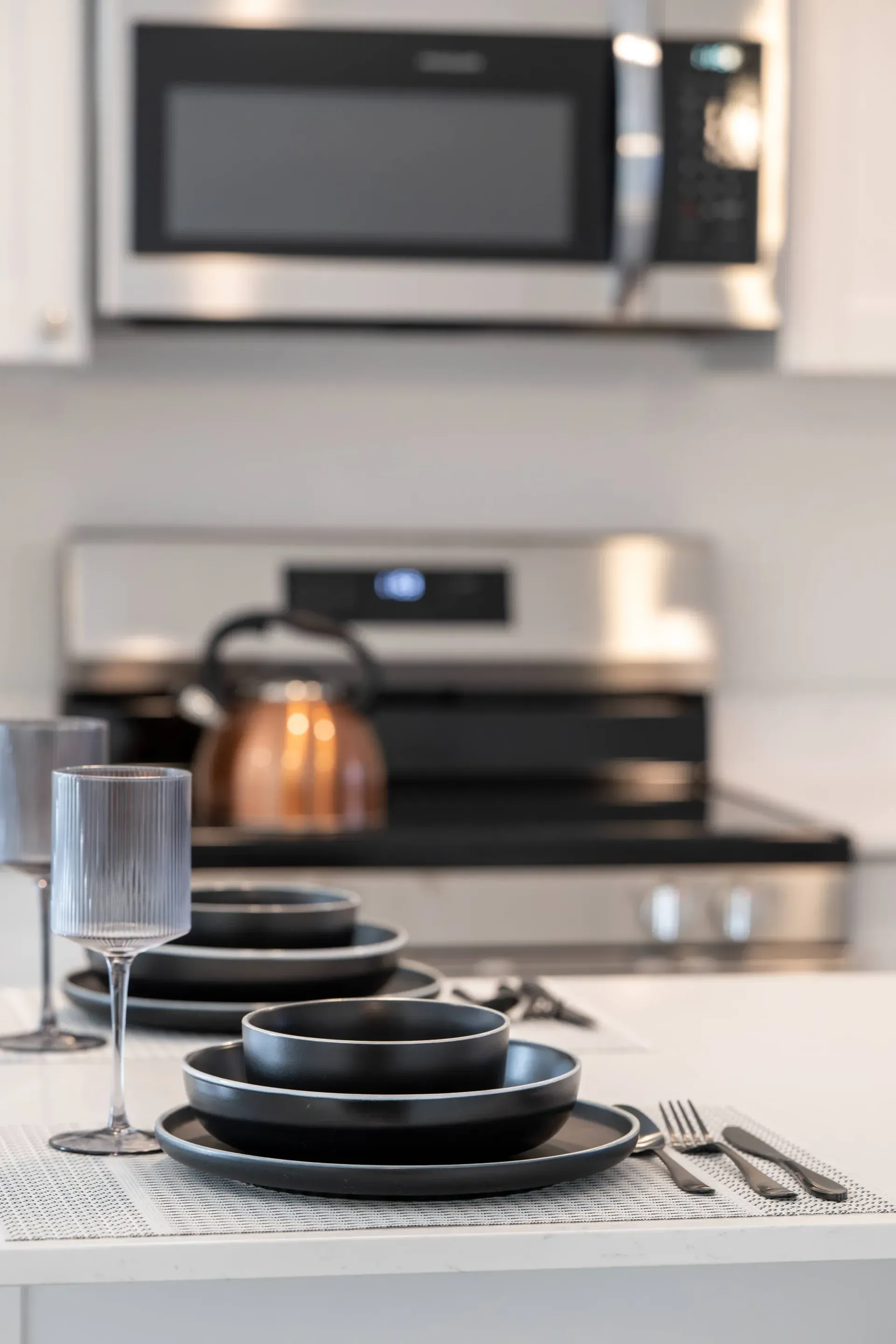 Modern apartment kitchen with white counter, black dishware, and stainless appliances.