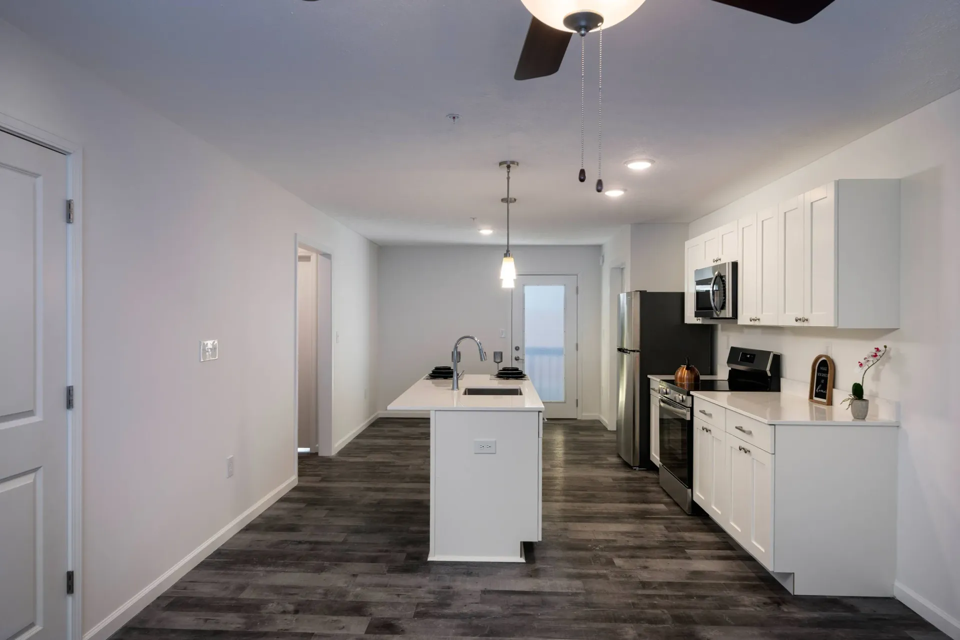 Bright kitchen in a modern apartment with an island, white cabinets, and stainless-steel appliances.
