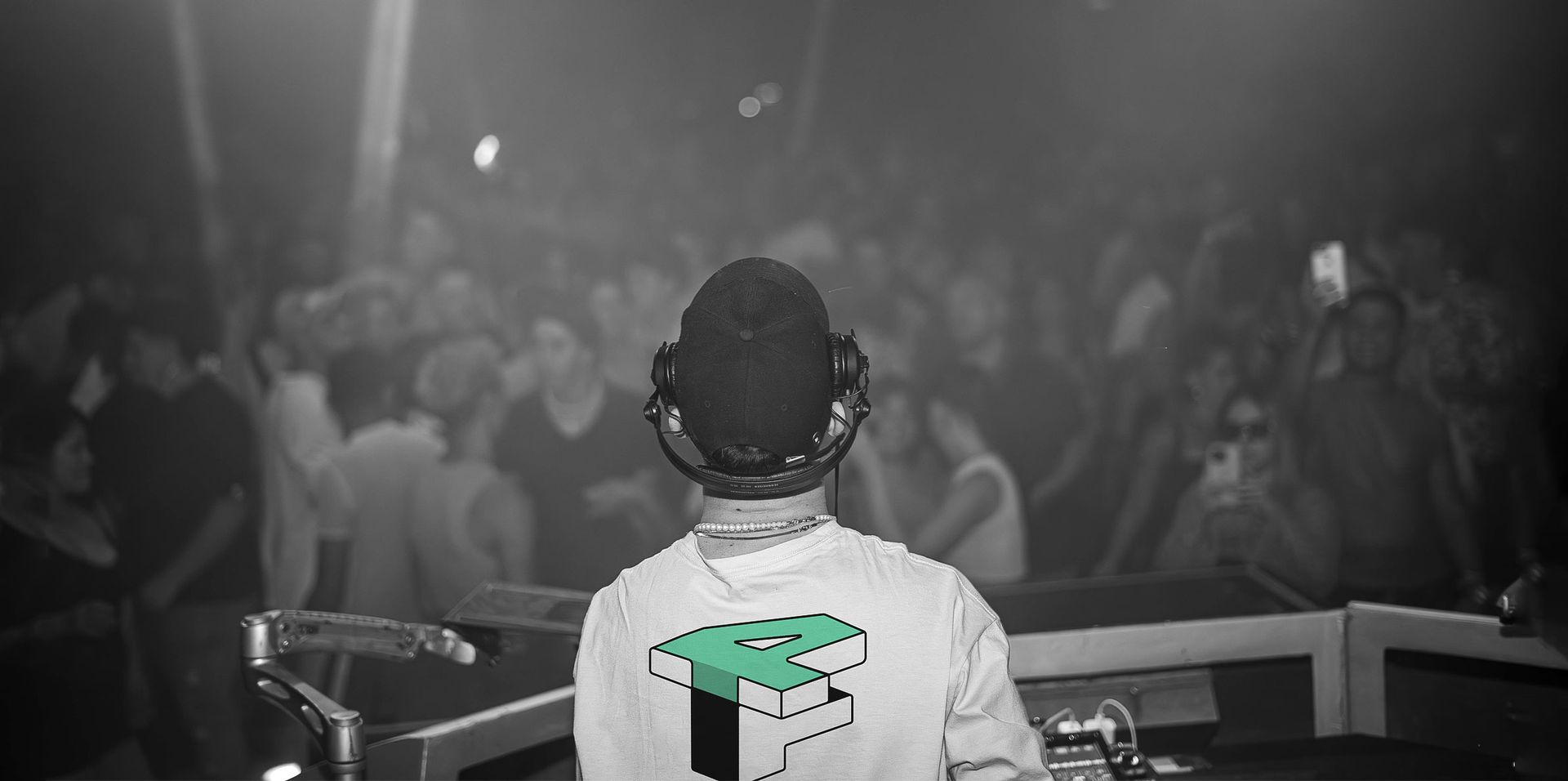 DJ seen from behind facing a crowd, with a green-lit console in a dark concert venue