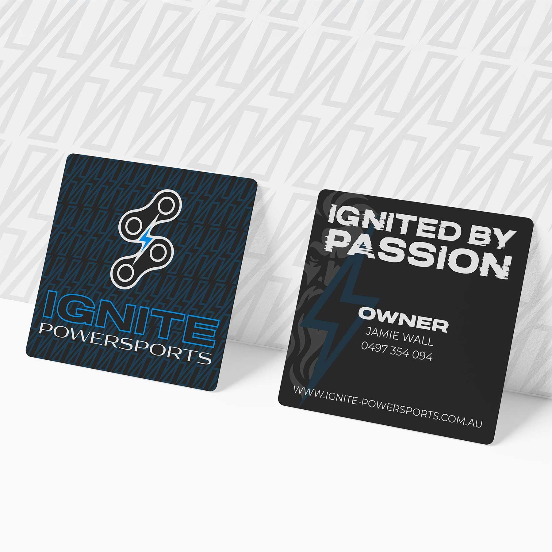 Two dark business cards on a light patterned surface, one with a logo, the other reading “IGNITED BY PASSION” and “OWNER”.
