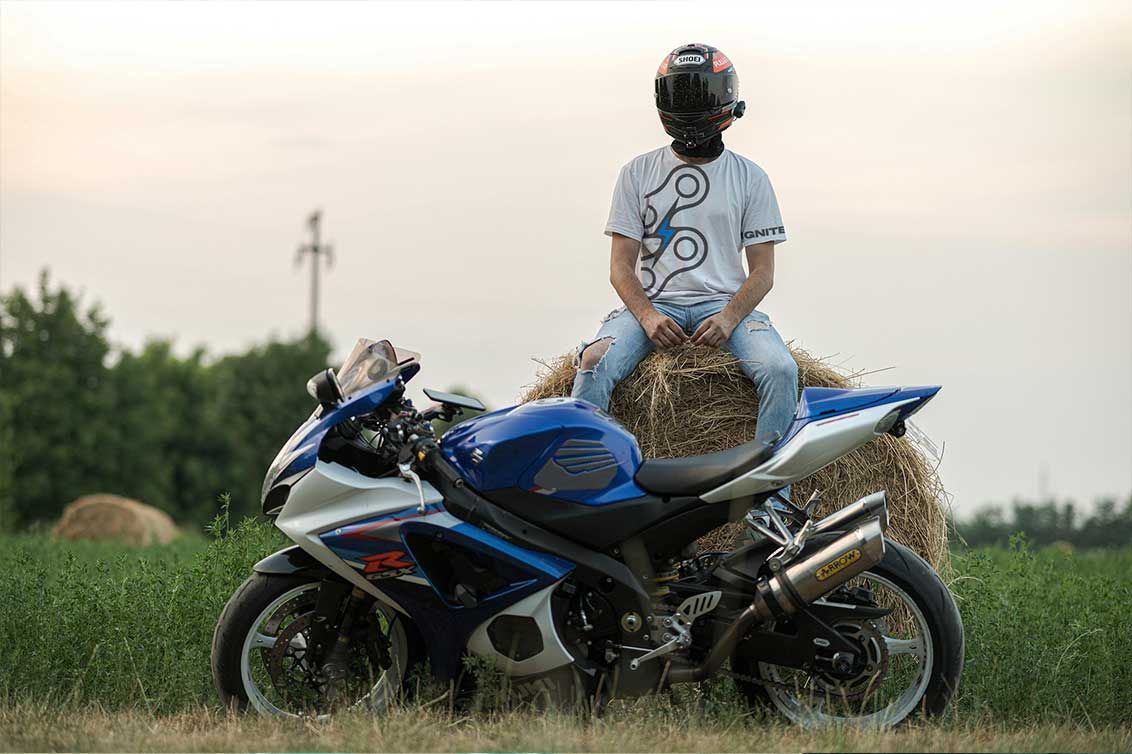Person sitting on a blue sport motorcycle in a grassy field at sunset