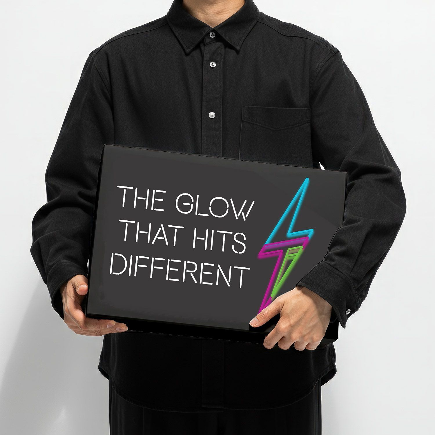 Person holding a black sign reading “THE GLOW THAT HITS DIFFERENT” with a neon lightning bolt.