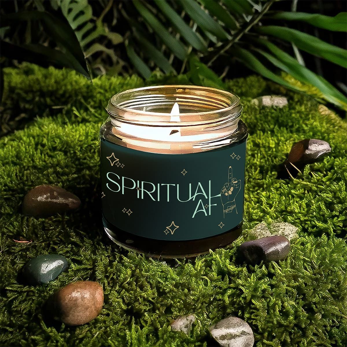 Green candle labeled “Spiritual AF” burning on moss with scattered stones and fern leaves