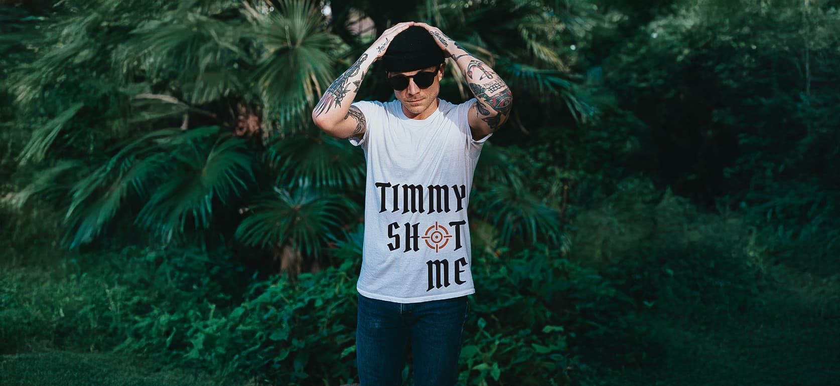 Person standing in lush greenery, forming a heart above their head, wearing a white shirt with bold text.