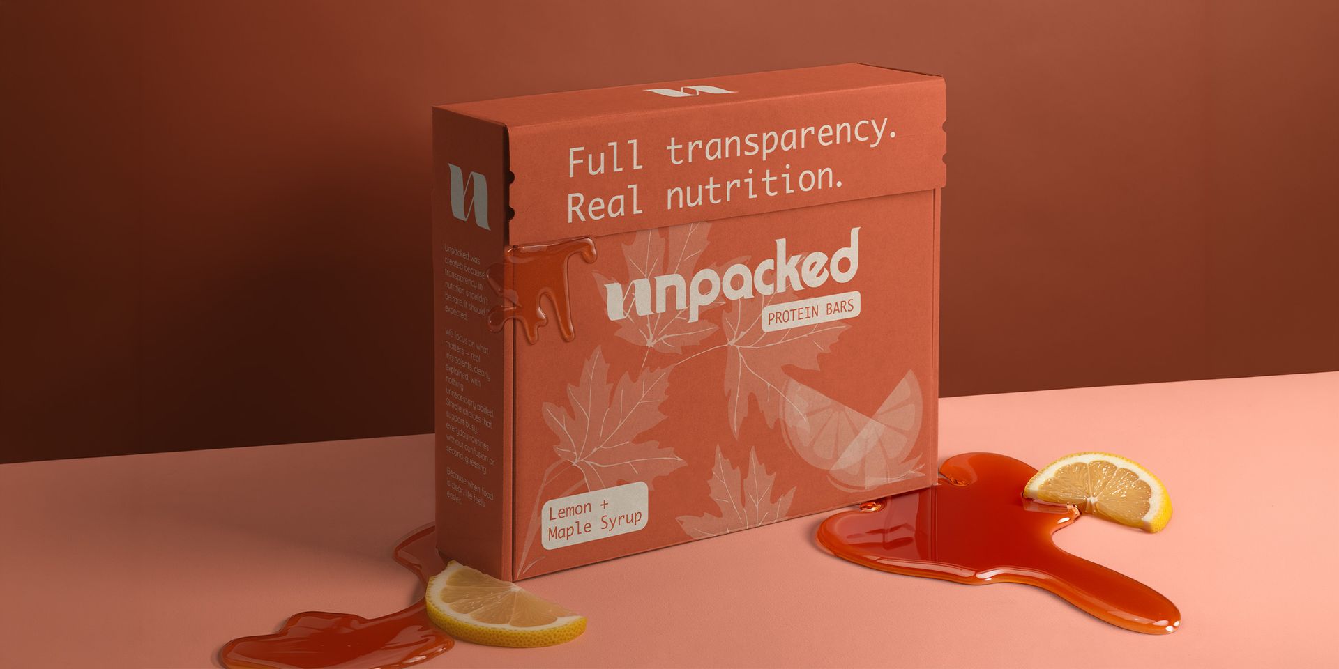 Orange snack box on a pink surface with spilled syrup and a spoon beside sliced fruit.