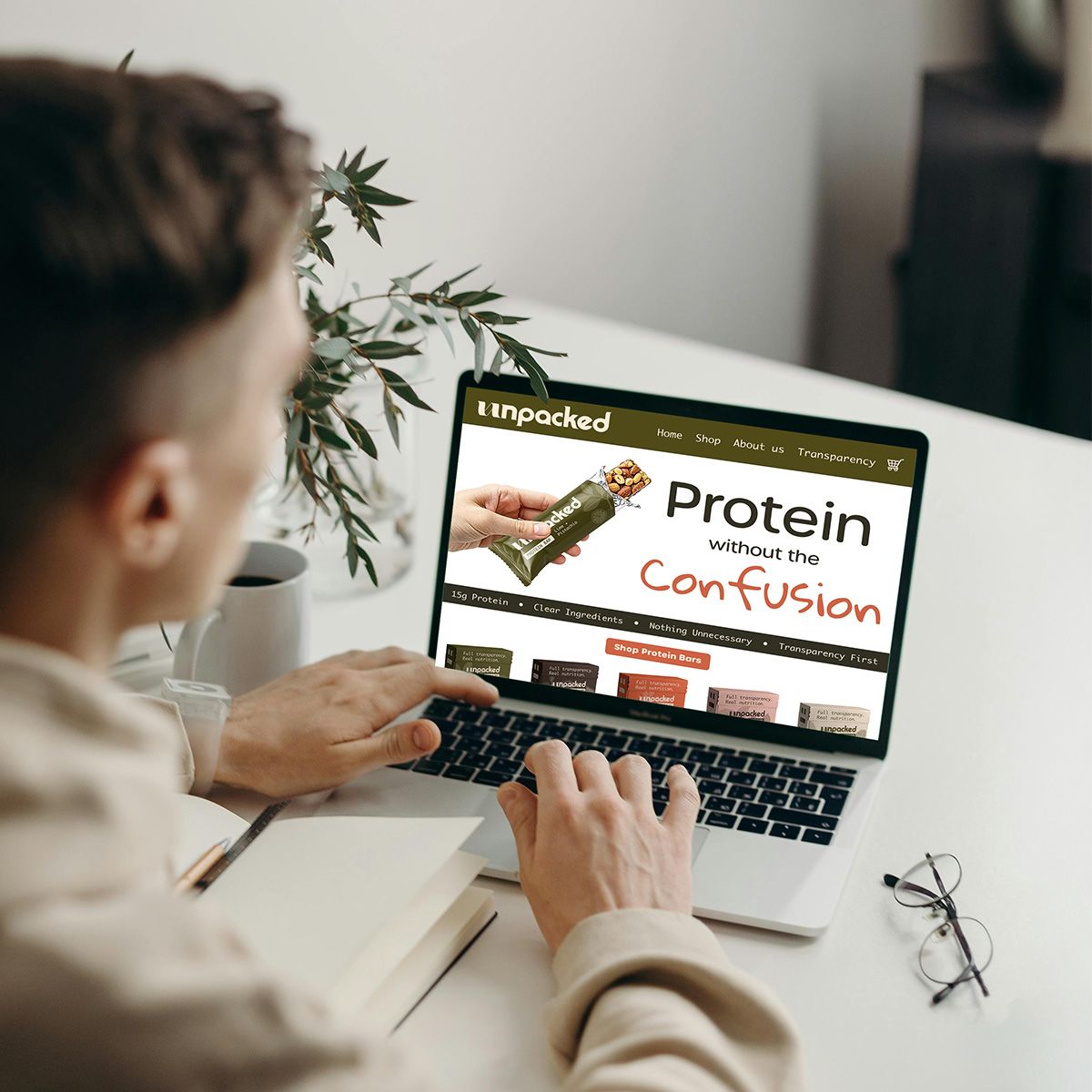 Person typing on a laptop showing a “Protein Confusion” webpage at a desk with a mug and plant