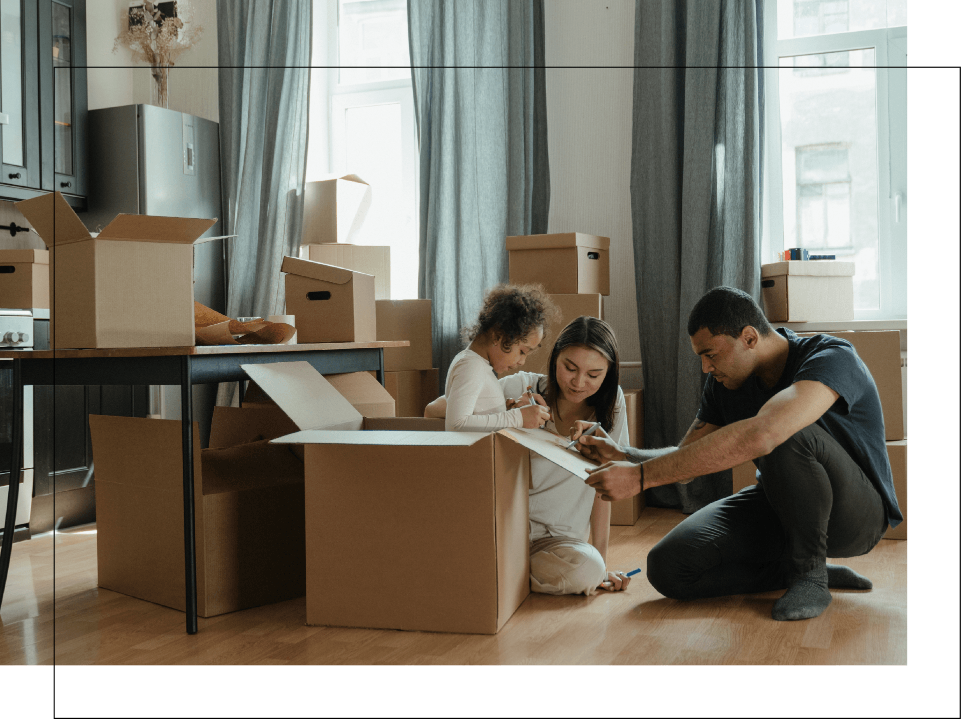 A family is sitting on the floor in a living room surrounded by cardboard boxes.