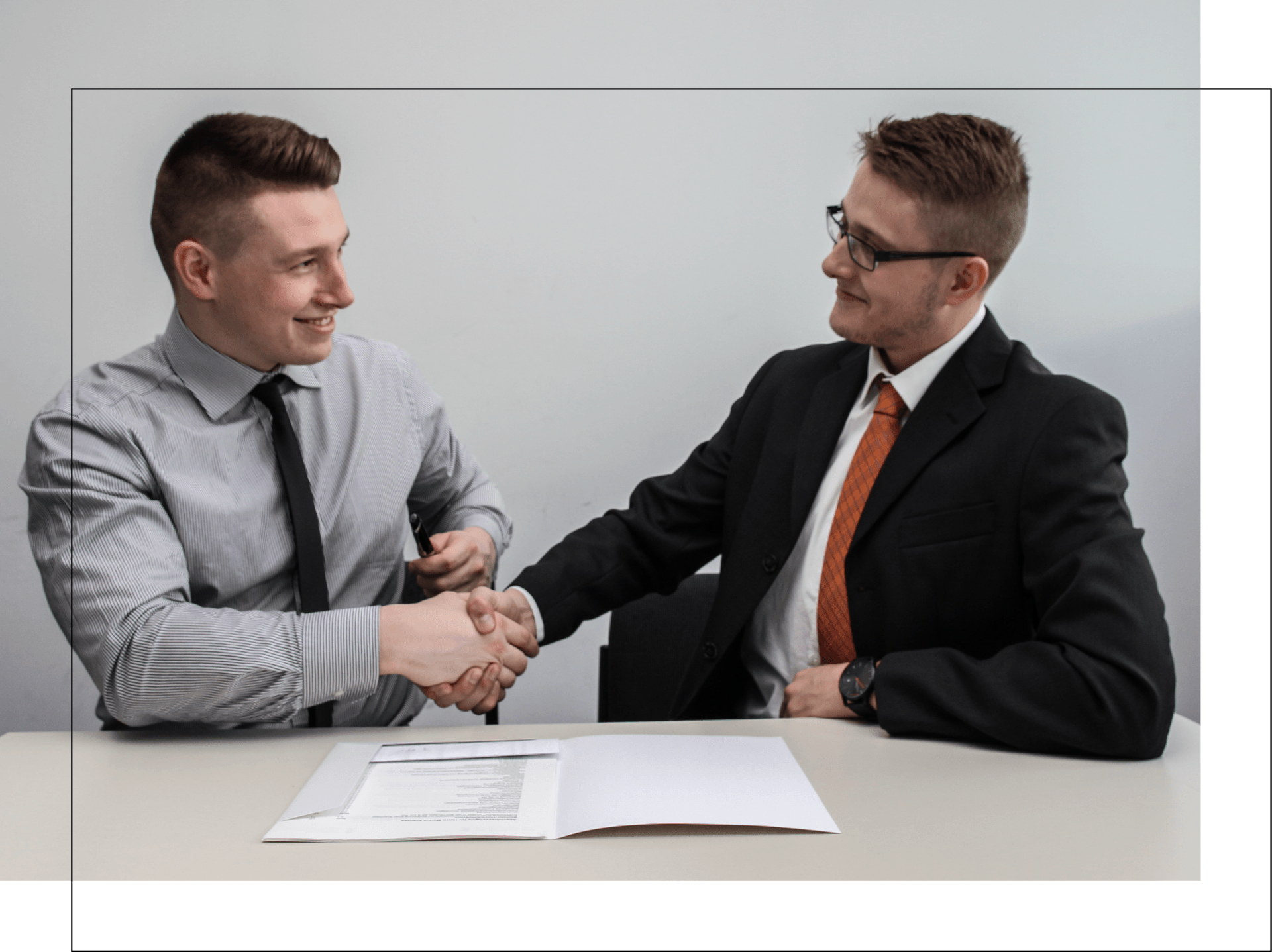 Two men are shaking hands while sitting at a table.