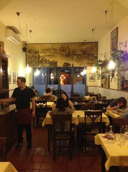 Accogliente interno del ristorante con clienti seduti ai tavoli e un cameriere che attraversa la sala.