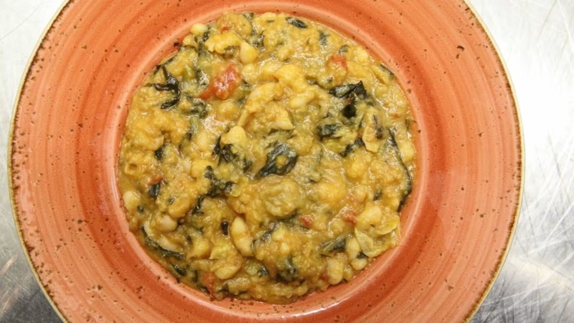 Ciotola di stufato con fagioli, pomodori e verdure su un piatto arancione.