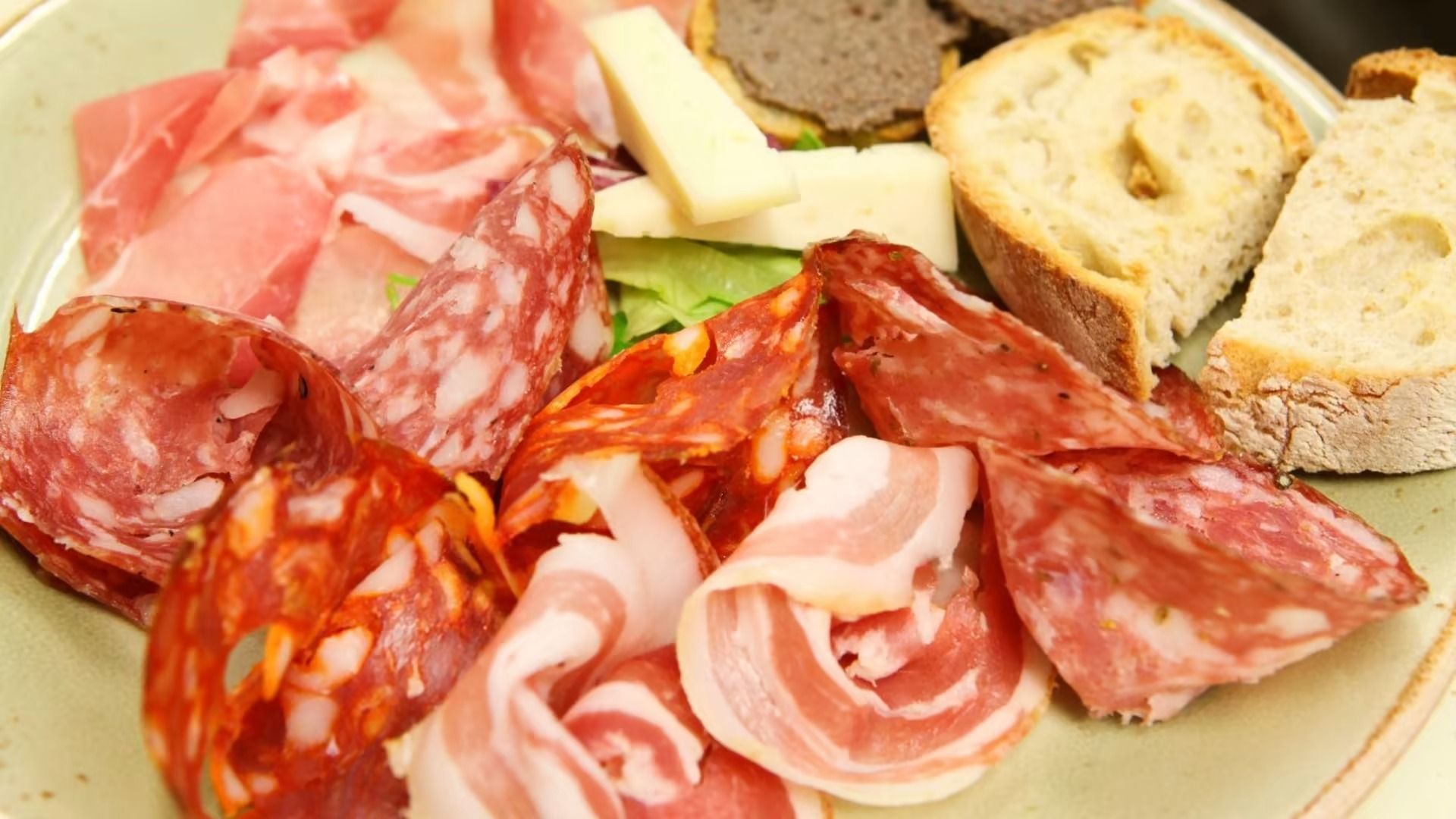 Piatto di salumi con salumi, formaggi e pane su un piatto verde.