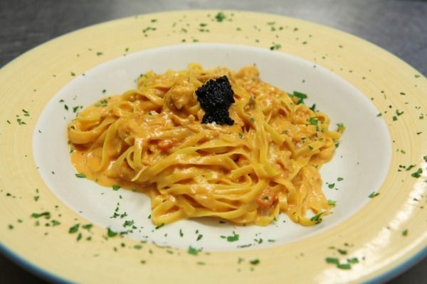 Piatto di pasta con salsa cremosa all'arancia, guarnito con caviale nero, servito su un piatto con bordo giallo.