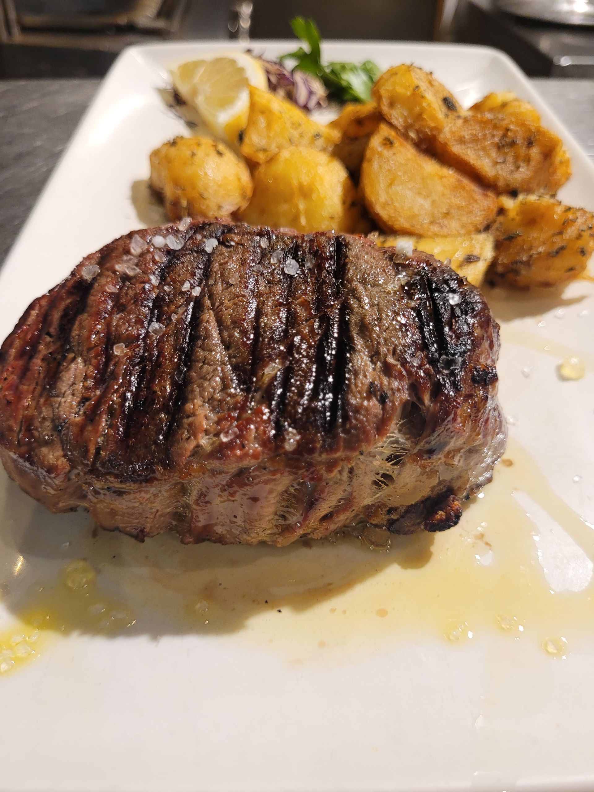 Bistecca alla griglia con patate arrosto e limone su un piatto bianco.