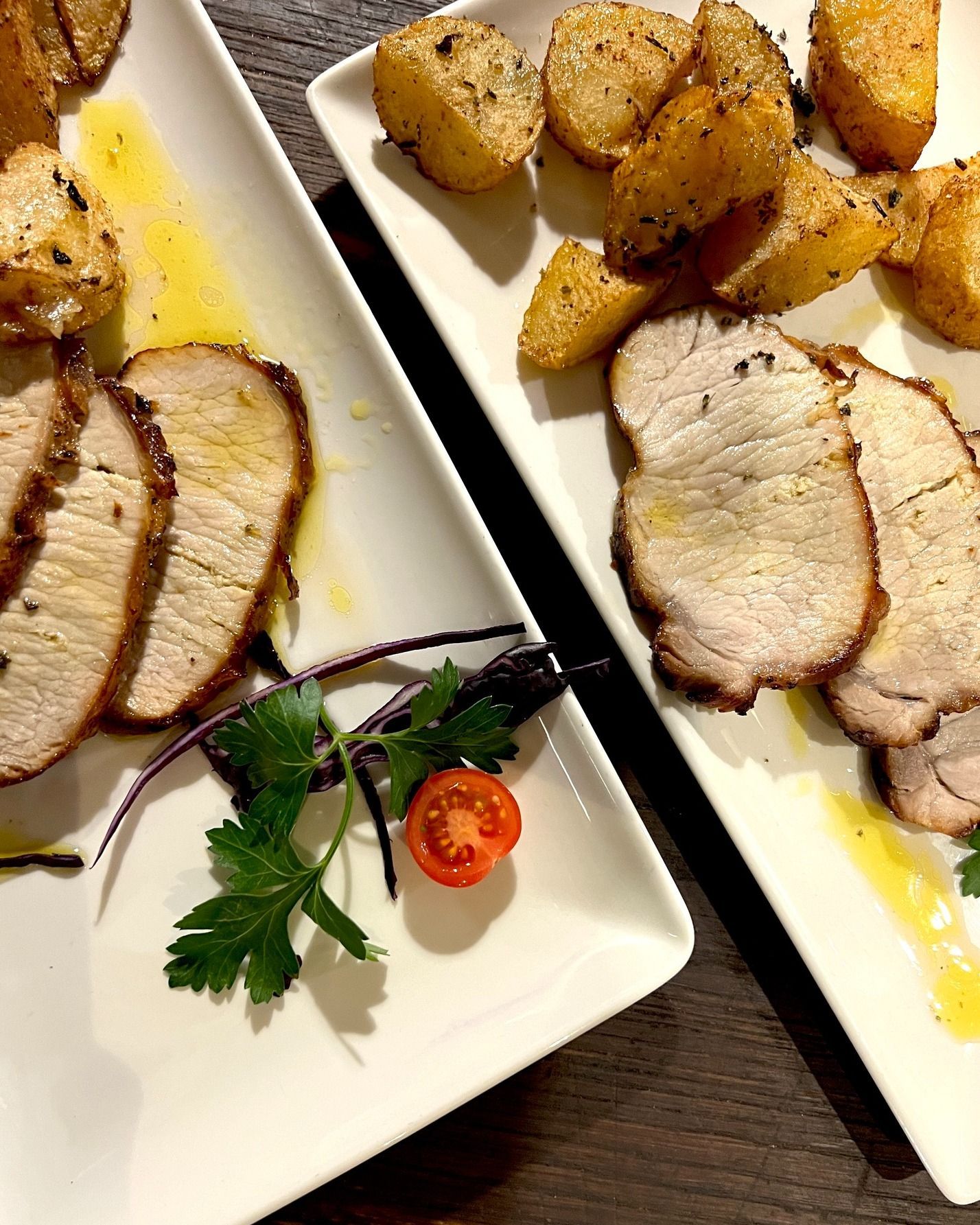 Due piatti di carne affettata, patate arrosto e guarnizione su un tavolo di legno.