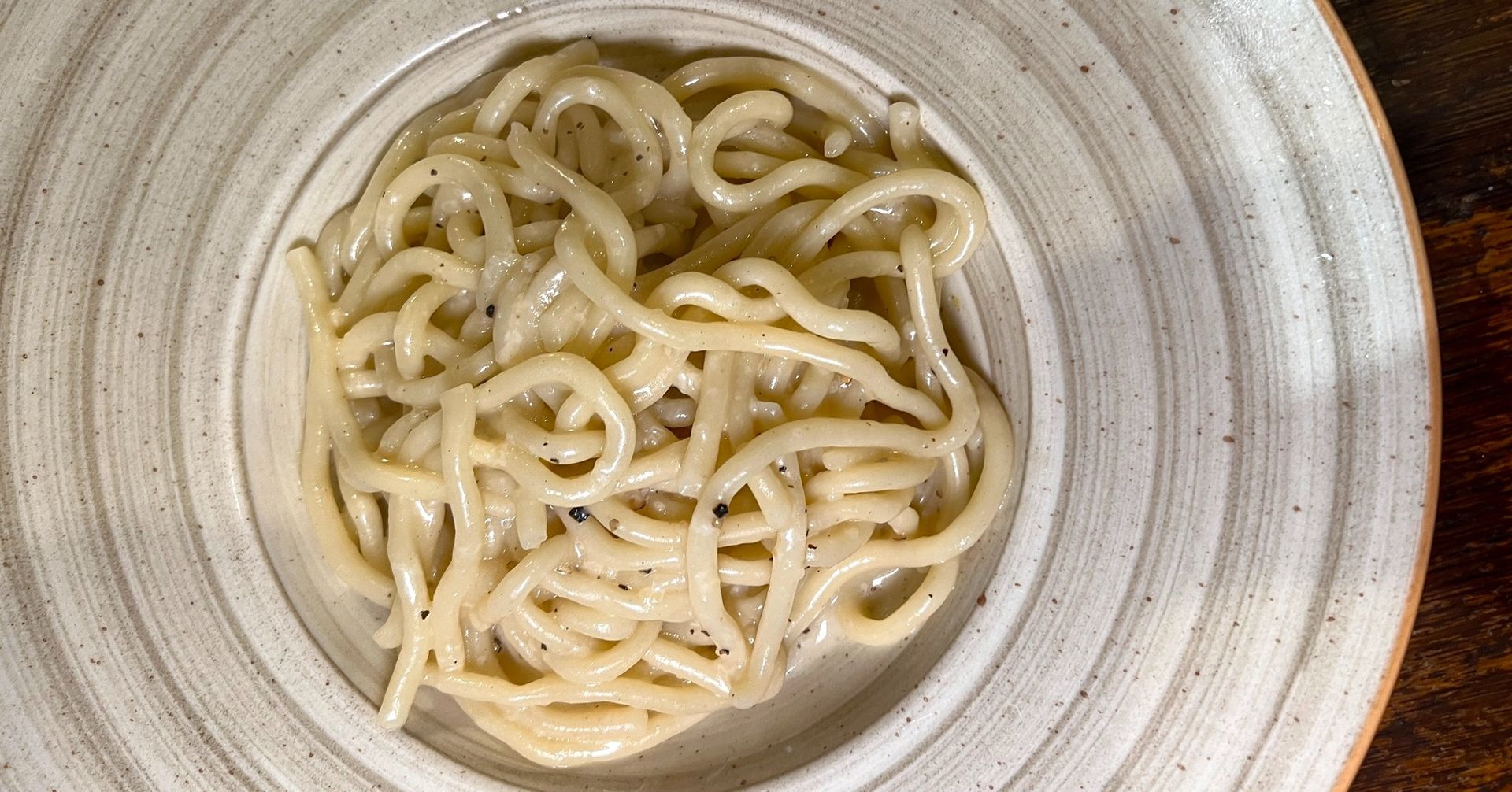 Un piatto di cremosa pasta cacio e pepe. Tagliatelle beige in una ciotola rustica e chiara.