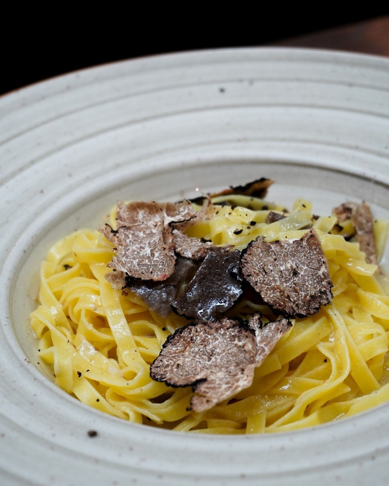 Piatto di pasta: fettuccine con tartufo nero grattugiato in una ciotola bianca.