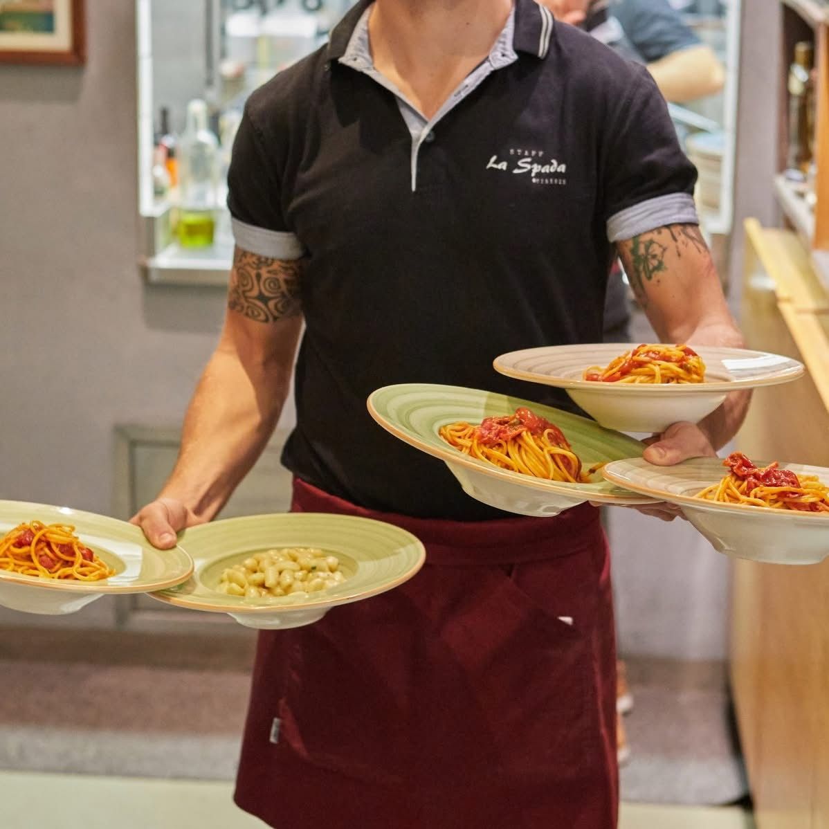 Cameriere che regge diversi piatti di pasta in un ristorante.