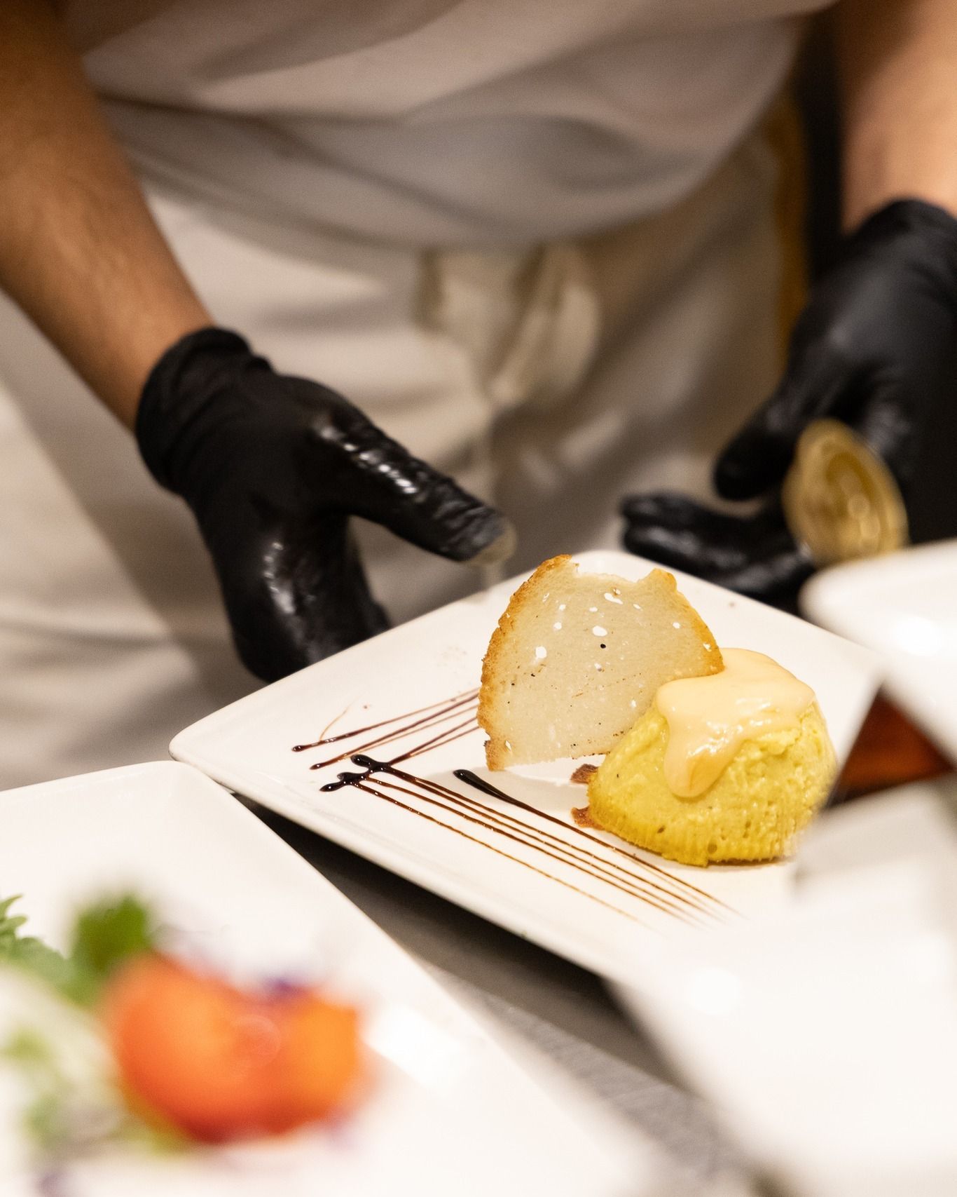 Chef che impiatta un piatto con pere, torta e glassa balsamica. Guanti neri.