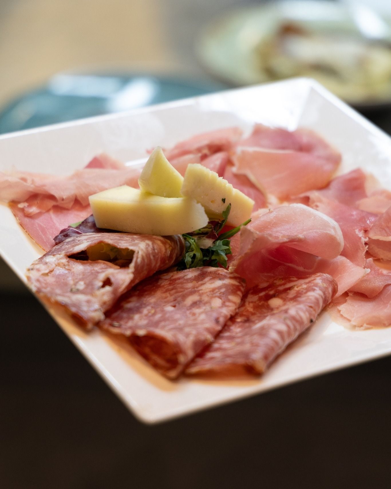 Piatto di salumi con affettati e formaggio su un piatto quadrato bianco.