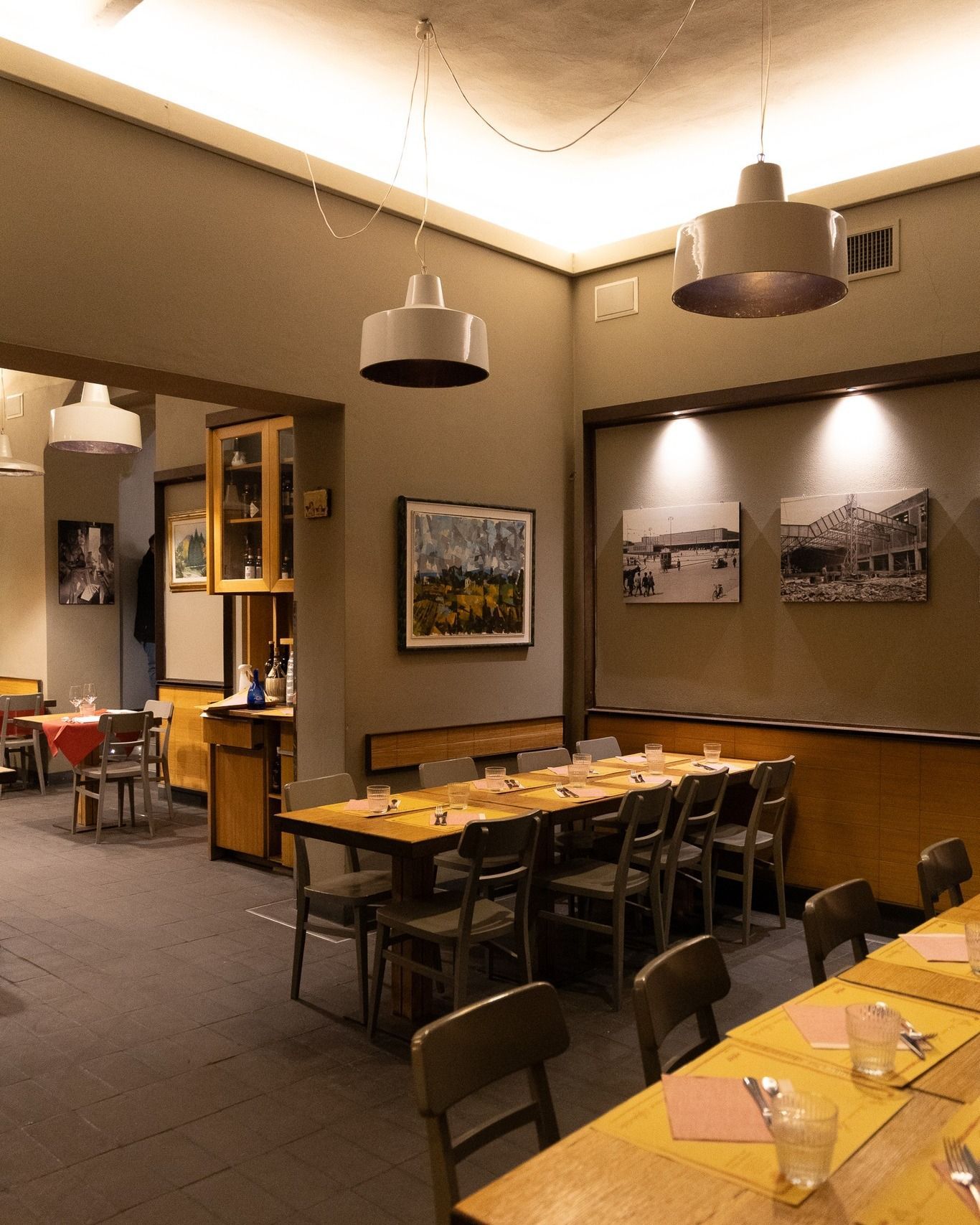 Interno del ristorante con lunghi tavoli, sedie, opere d'arte e lampade a sospensione.