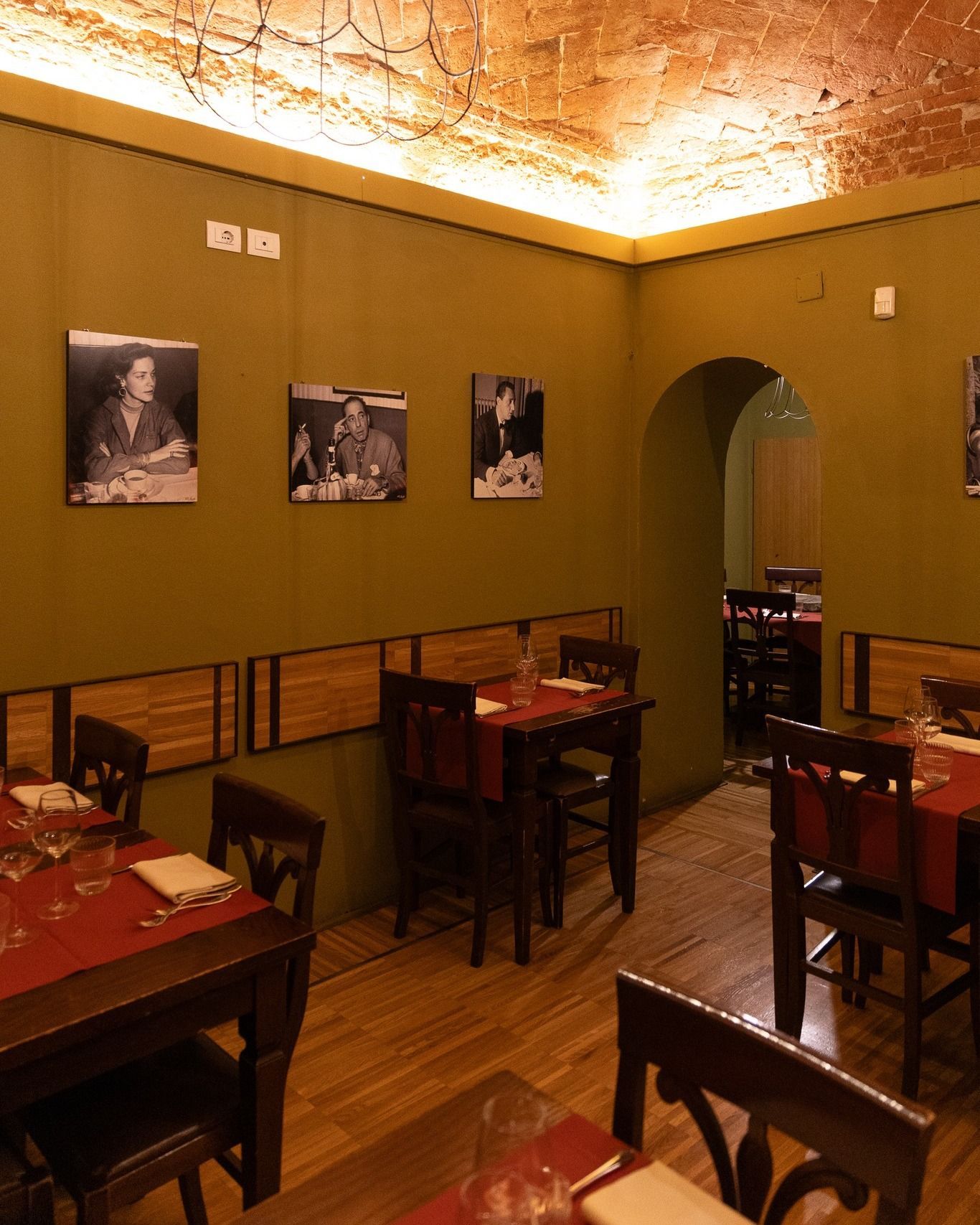 Interno del ristorante con pareti verde oliva, tavoli con tovaglie rosse, sedie in legno e foto in bianco e nero.