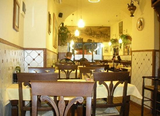 Accogliente interno di un caffè con tavoli in legno, luci gialle calde e pareti piastrellate.