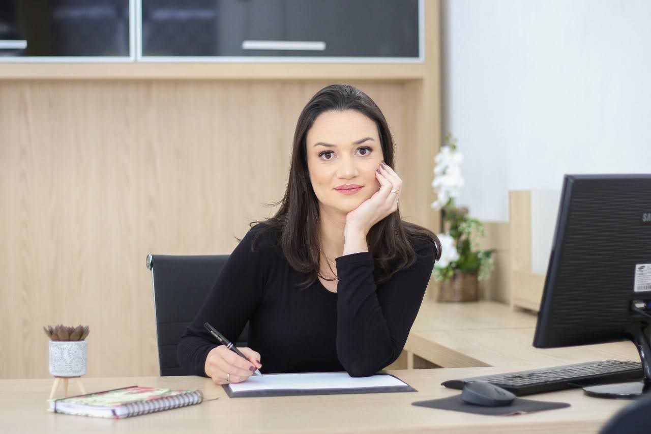 Uma mulher está sentada em uma mesa em frente a um computador.