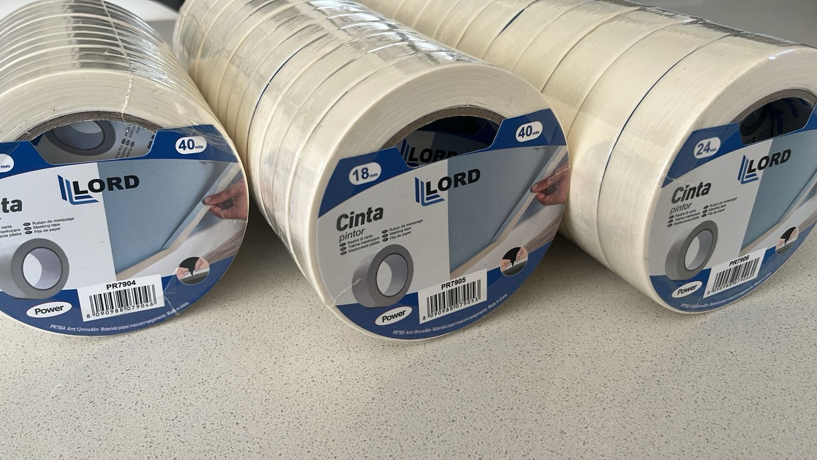 Rollos de cinta de enmascarar marca LORD sobre una superficie blanca. Los rollos están envueltos en plástico transparente.