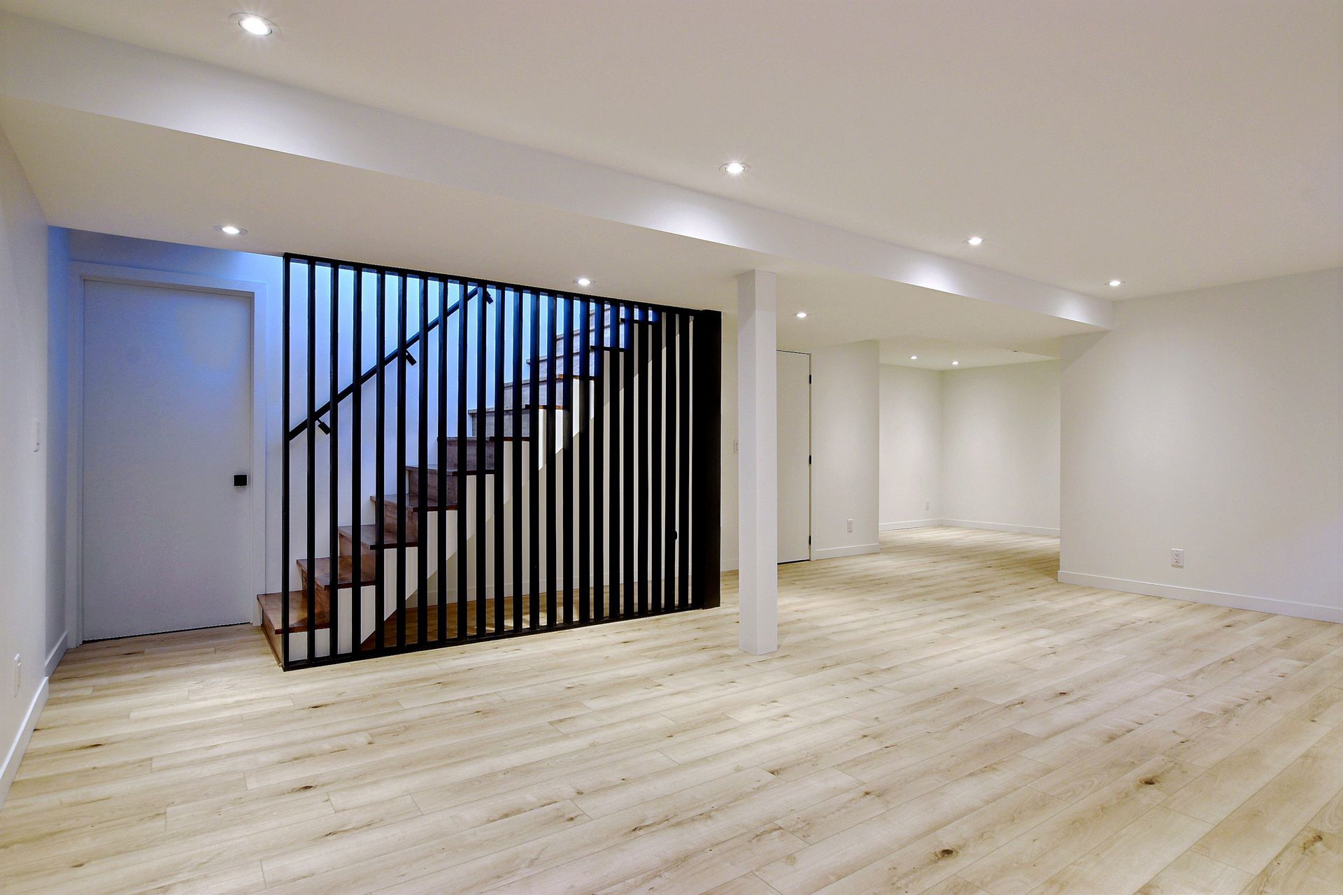 Sous-sol rénové avec plancher de bois, escalier noir et murs blancs.