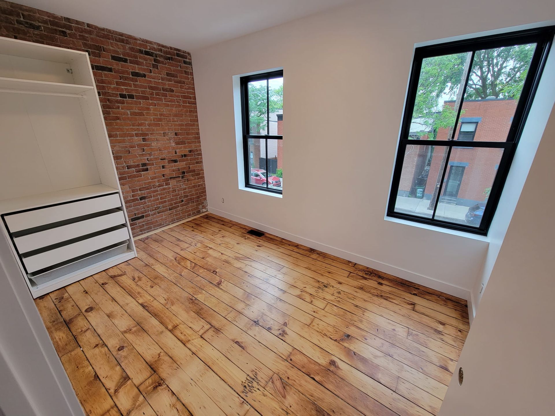 Une pièce vide avec du parquet et un mur en briques.