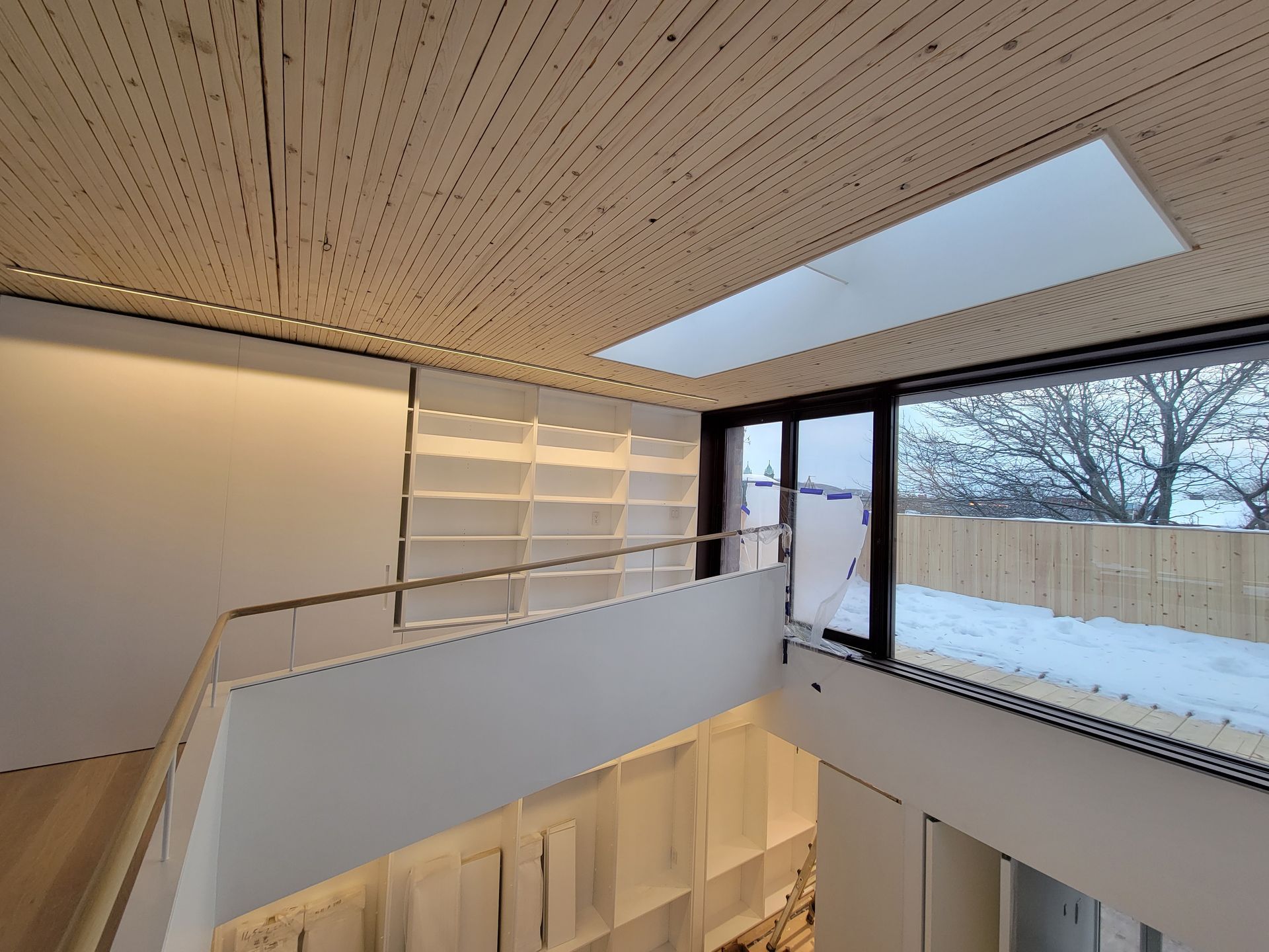 Intérieur d'une mezzanine avec escalier, rampe métallique, grandes fenêtres et plafond en bois.