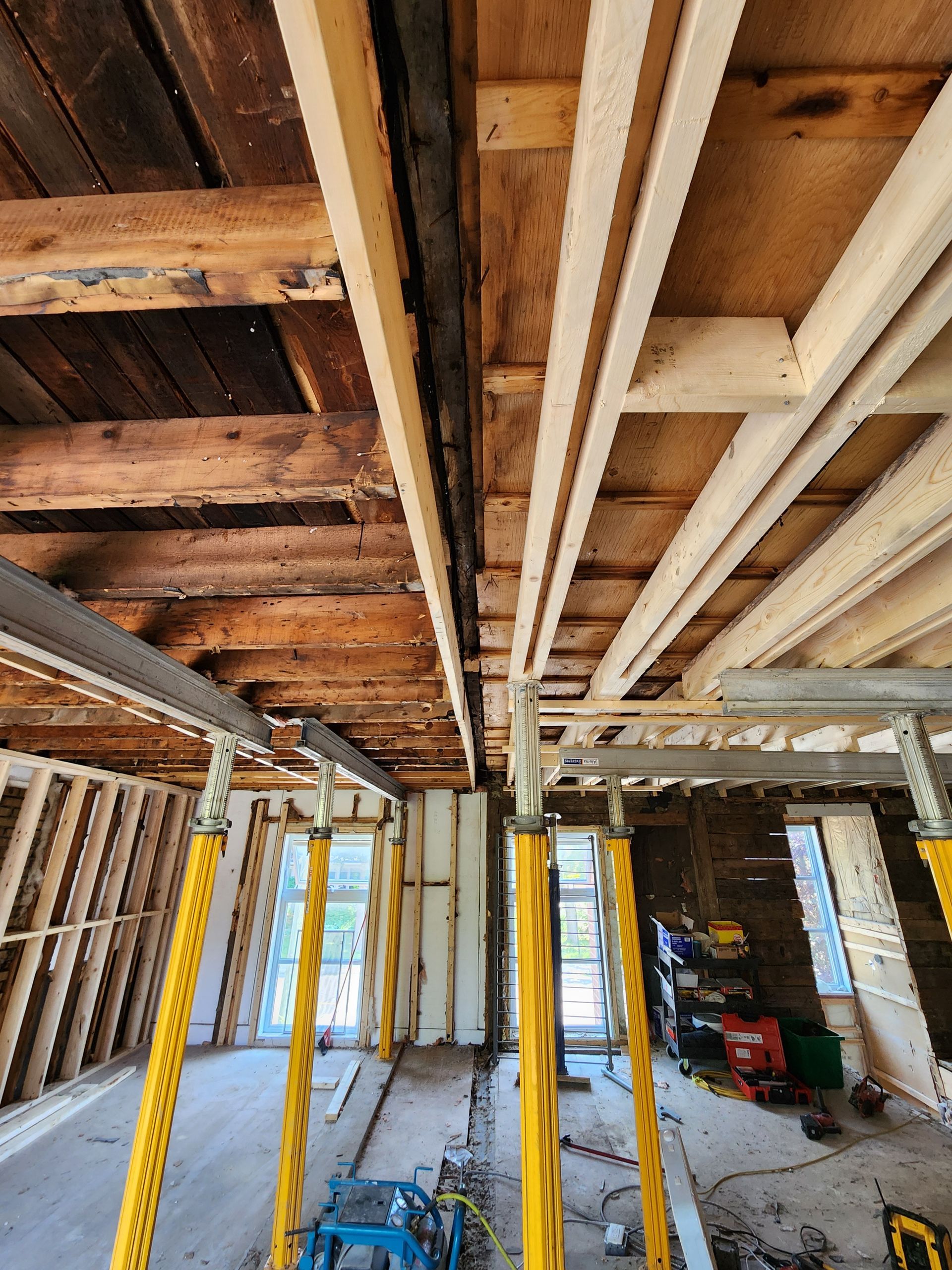 Intérieur d'un bâtiment en rénovation avec poutres apparentes et colonnes de support jaunes.