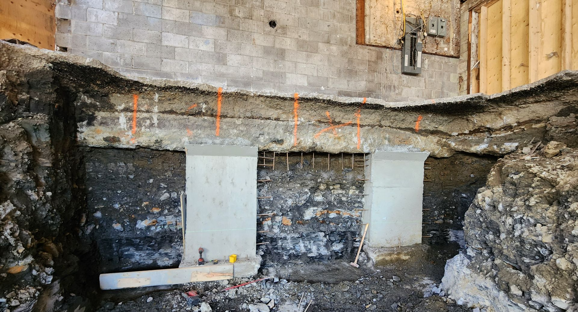 Mur de sous-sol avec imperméabilisation noire, taches blanches et réparations de fondations en béton apparentes.