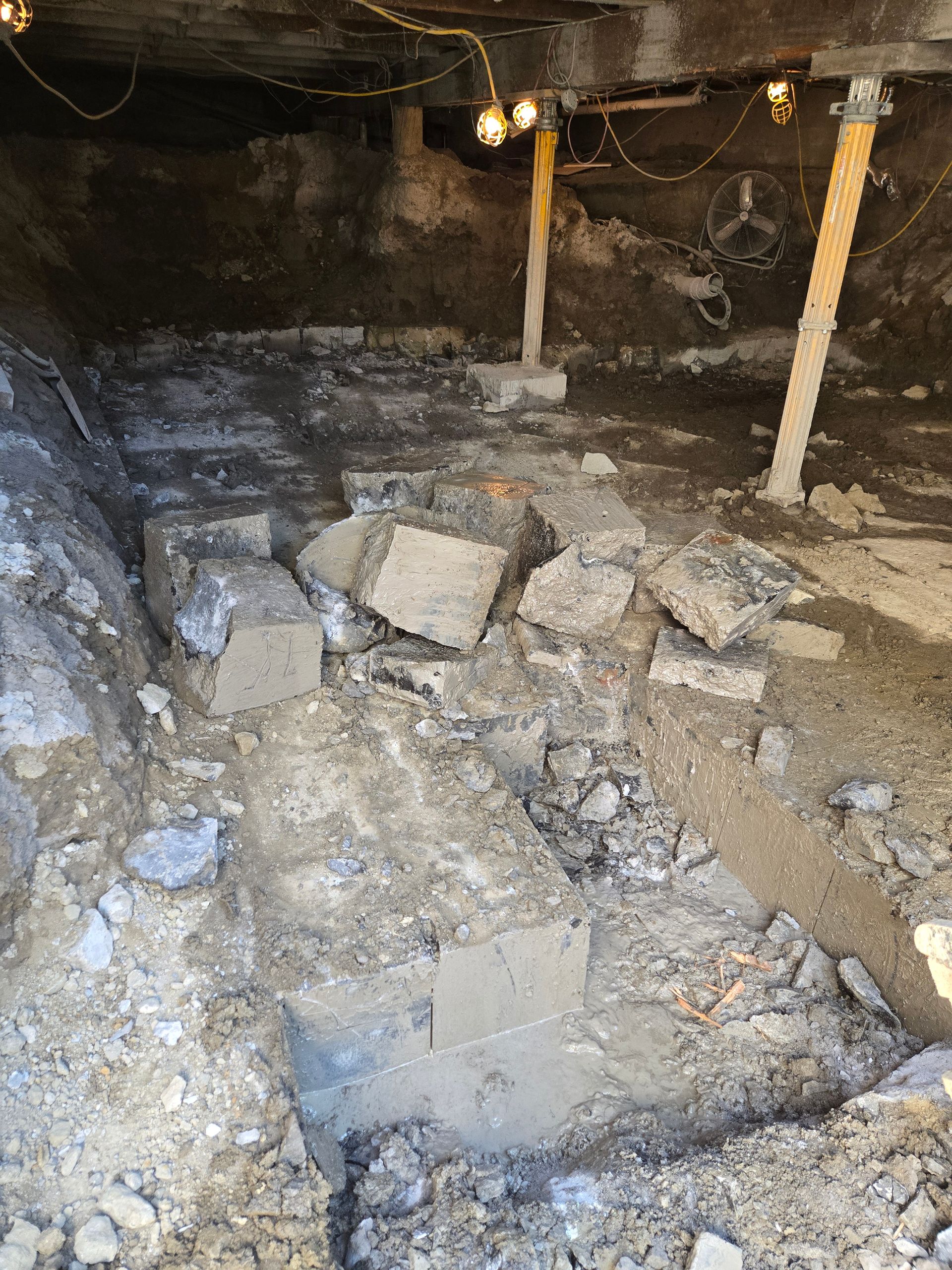 Sous-sol effondré avec des décombres, des blocs de béton brisés et des poteaux de soutien apparents sous un plafond bas.