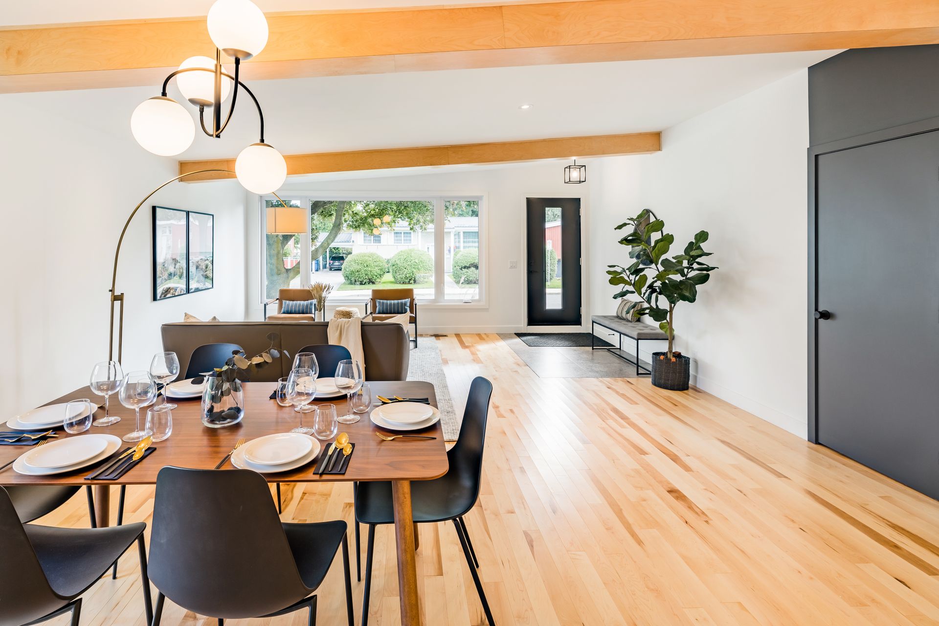 Salle &agrave; manger et salon d'une maison r&eacute;nov&eacute;e avec poutres apparentes, table en bois et baies vitr&eacute;es.