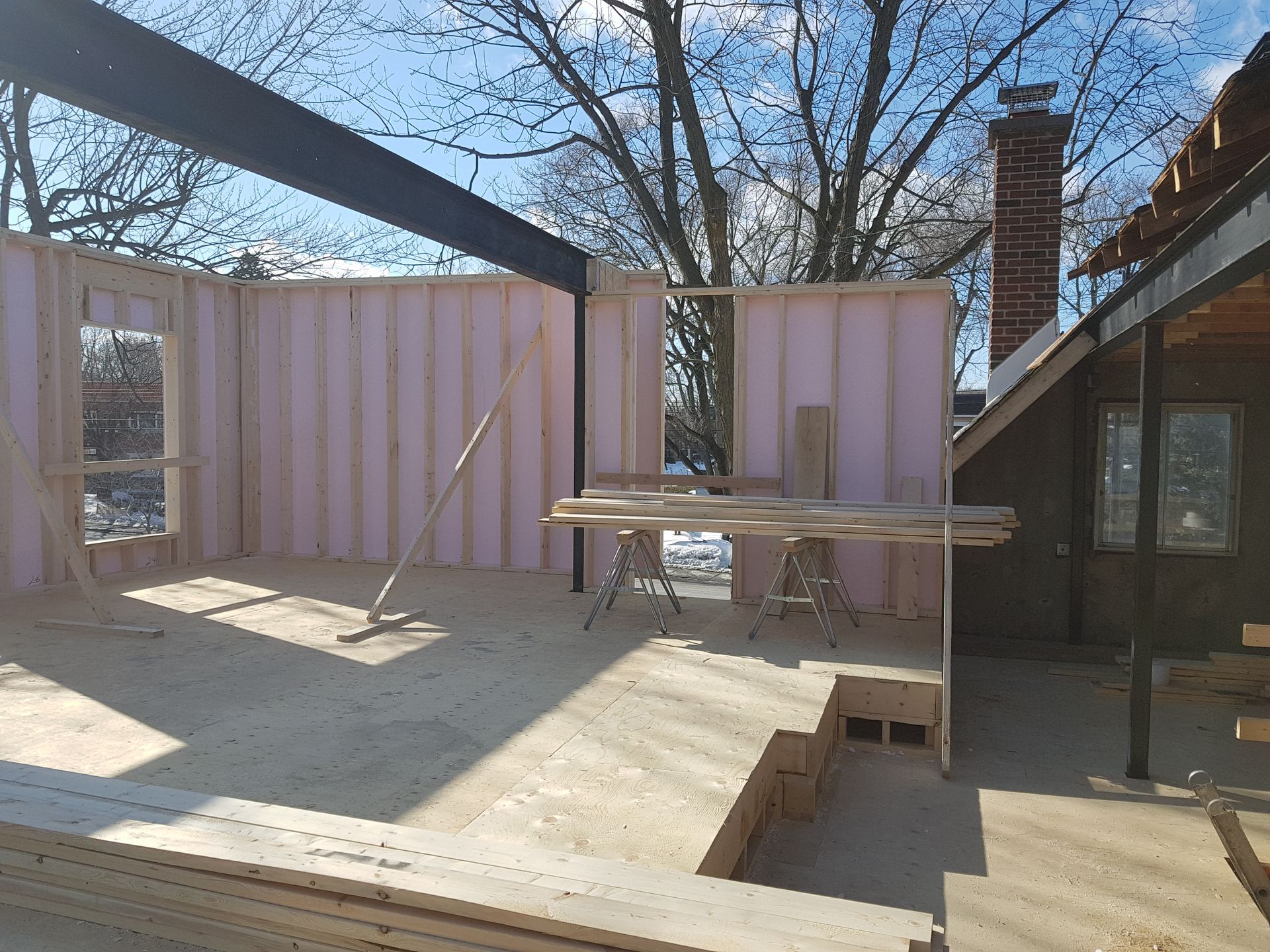 Construction site: framed walls, steel beams, pink insulation, wood flooring, and a brick chimney.