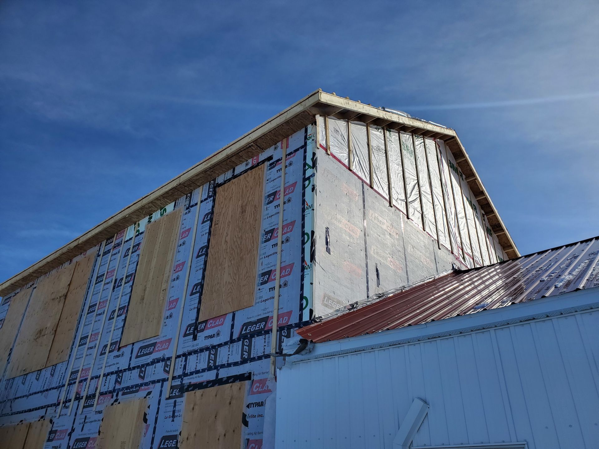 Grange en construction avec charpente de bois exposée et matériaux de revêtement contre un ciel bleu.