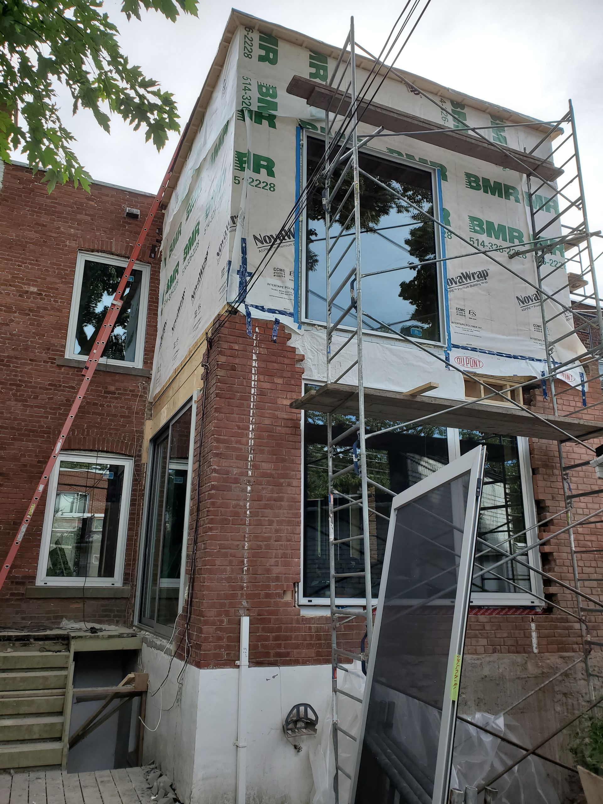 Two-story brick building under construction with scaffolding and new windows. Blue sheathing and red bricks.