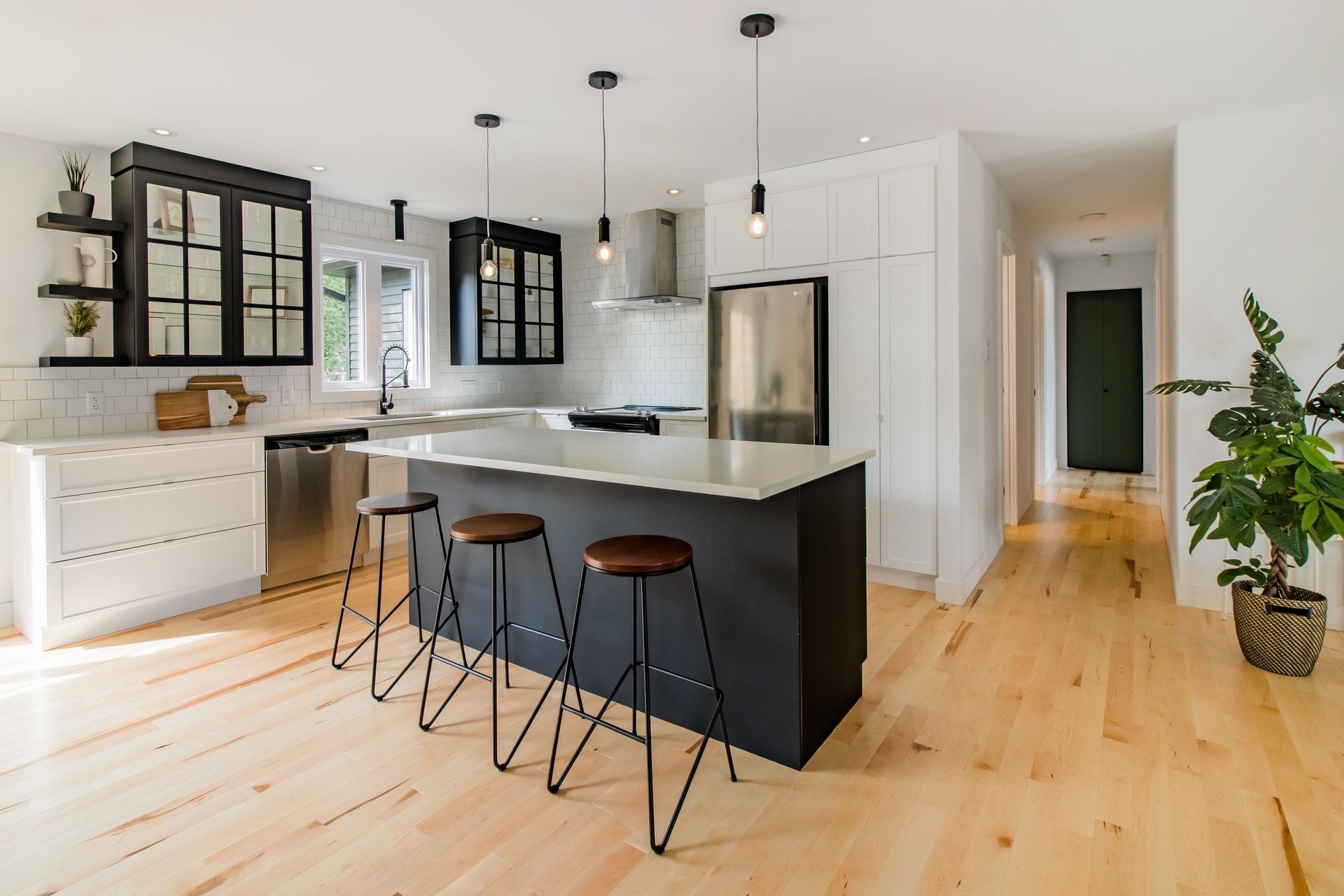 Cuisine moderne avec &icirc;lot central noir, armoires blanches et noires, appareils acier inoxydable et plancher bois.