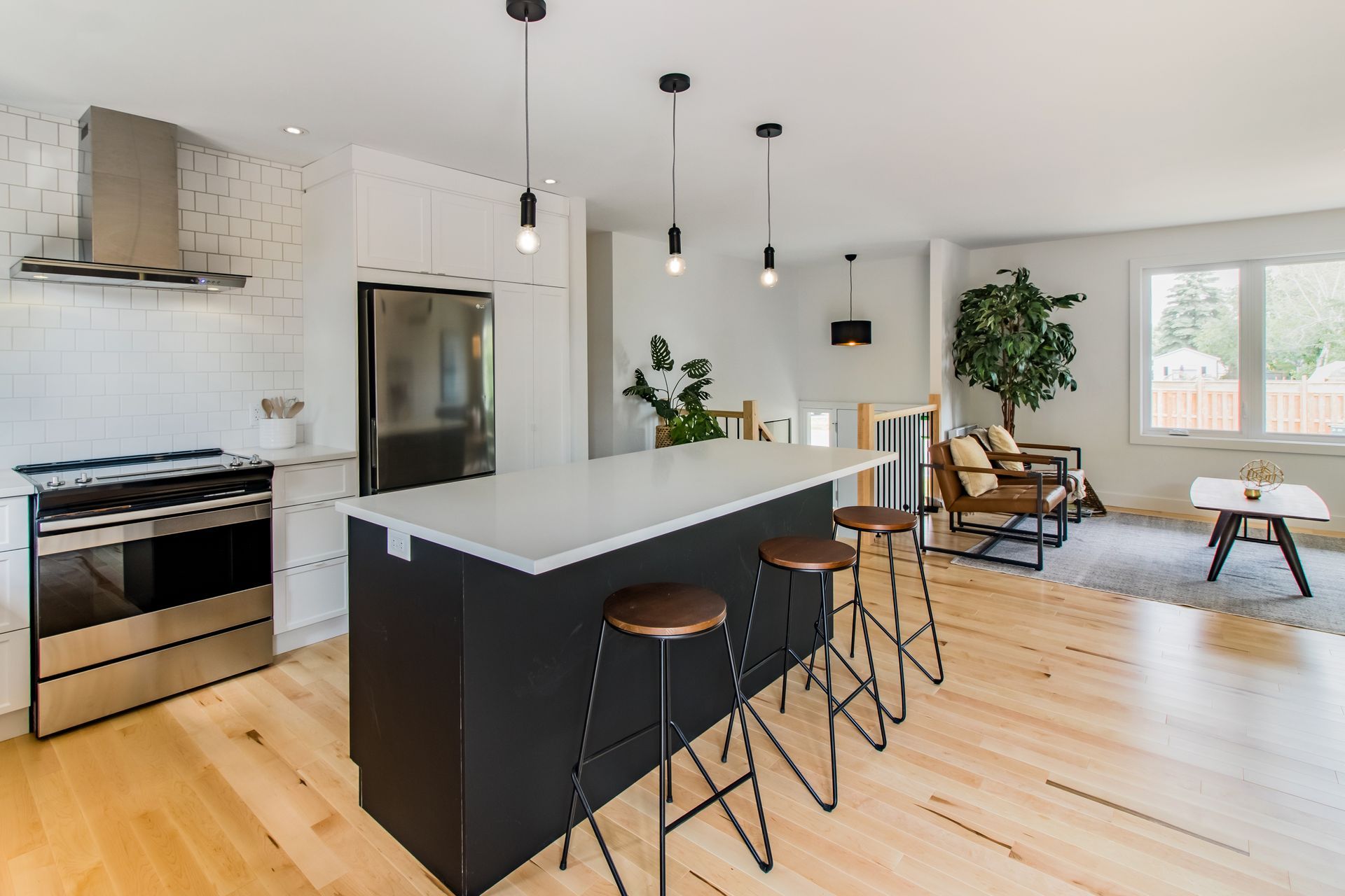 Cuisine moderne ouverte avec îlot central noir, tabourets de bar et coin salon lumineux avec plantes et chaises