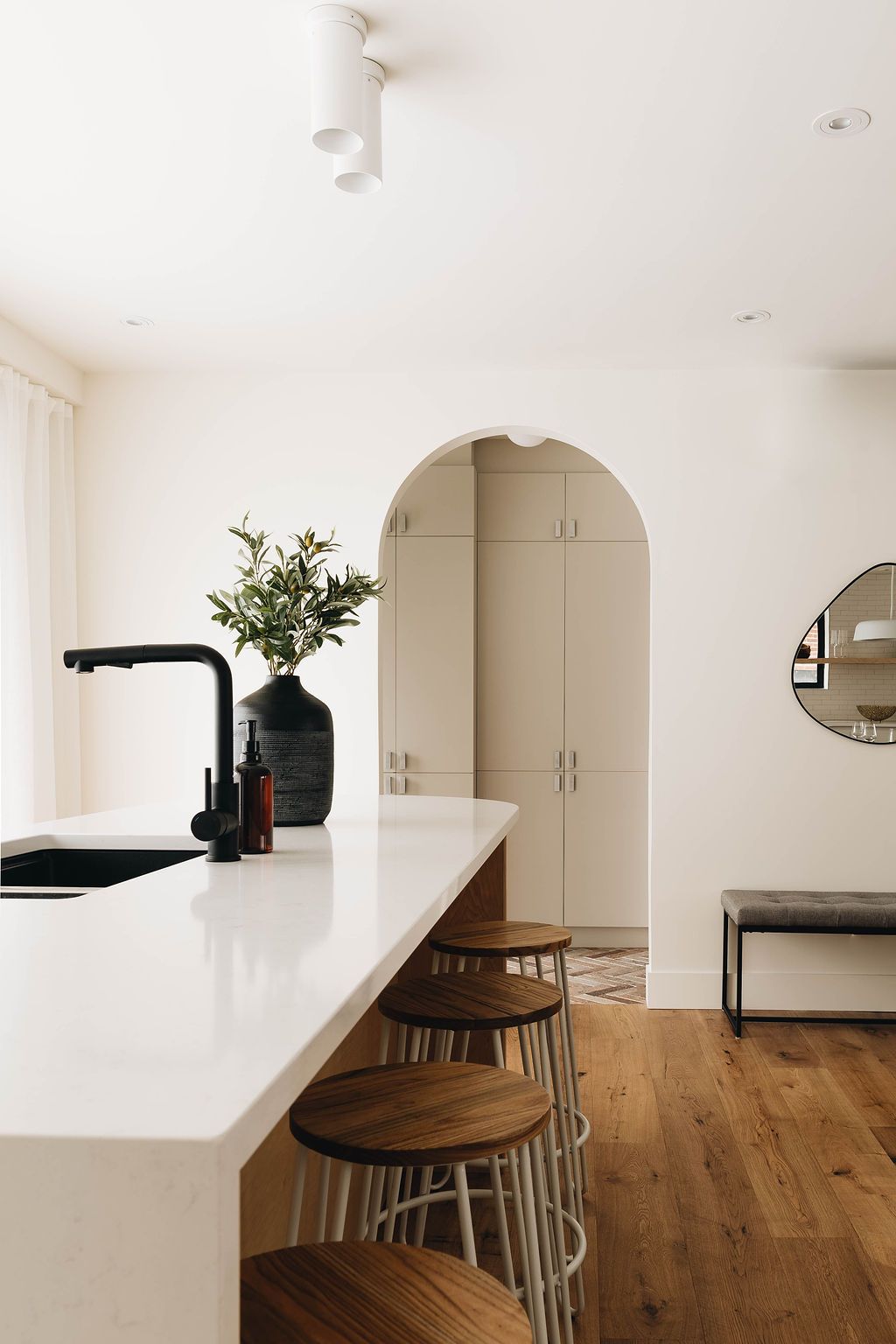 Une cuisine avec un comptoir blanc, des tabourets, un évier et un miroir.